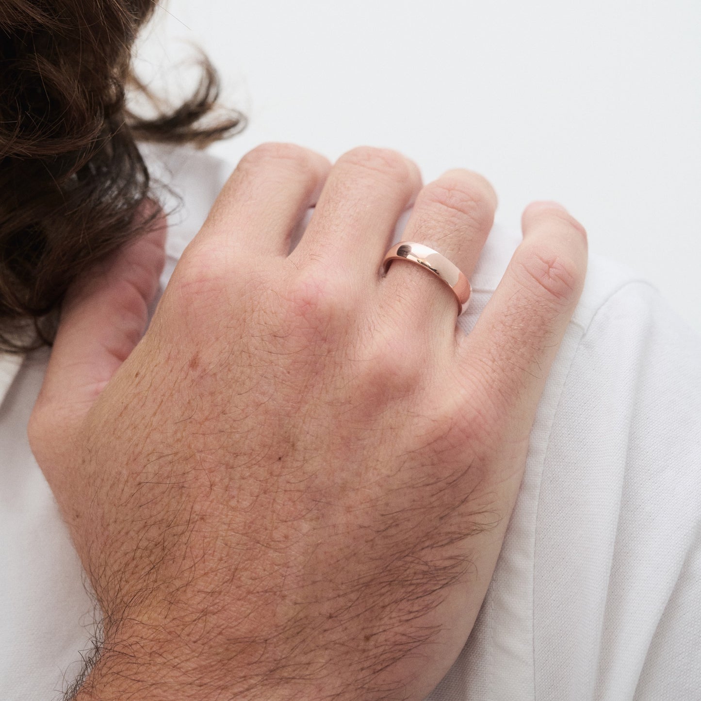 Man's hand wearing a polished rose gold ring, showcasing luxury jewellery. Hand rests on a white shirt. [text overlay: 5mm Polished Finish in Rose Gold]