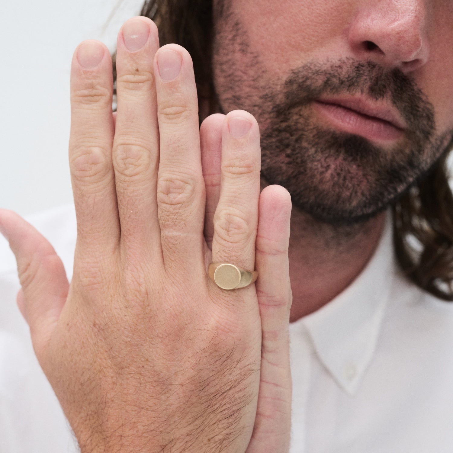 Man wearing a gold signet ring, showcasing it against his hand, white shirt visible. Luxurious jewellery detail.