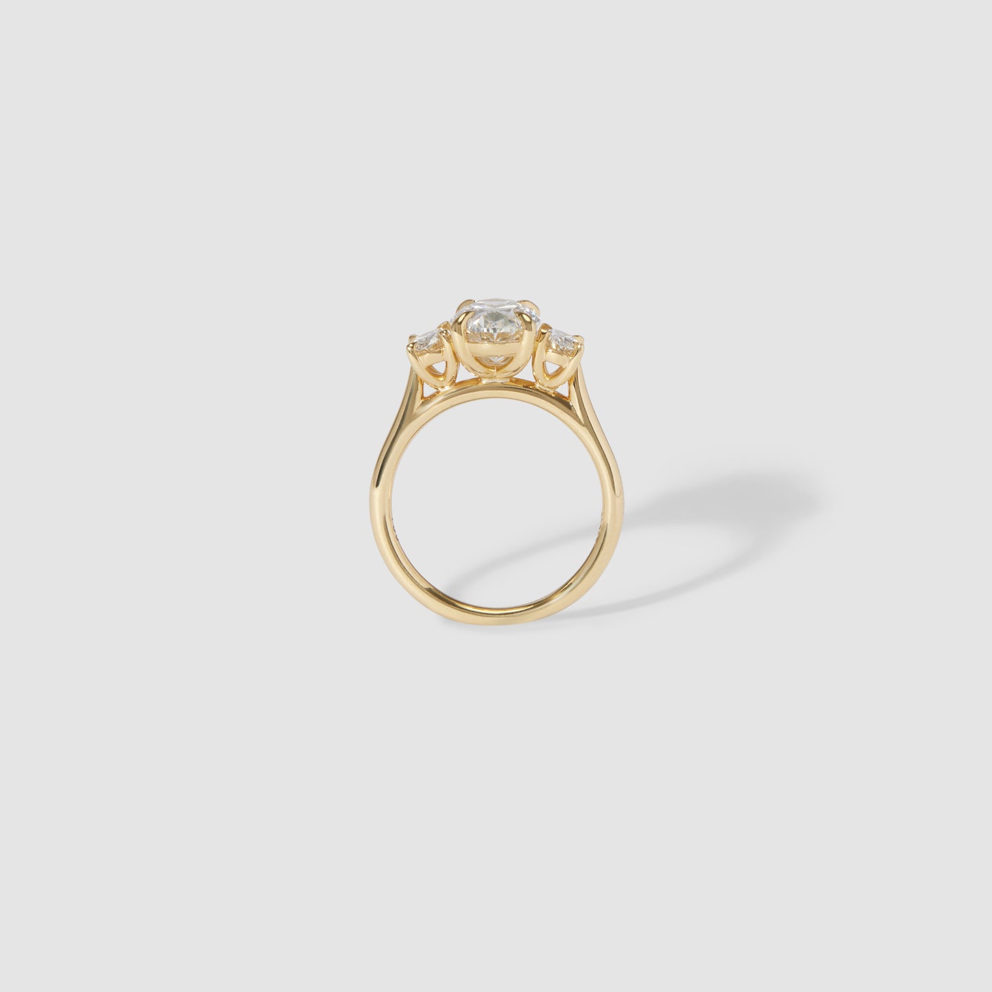 Gold engagement ring with a round brilliant diamond centre and two side stones, set in a high-profile, minimalist design.