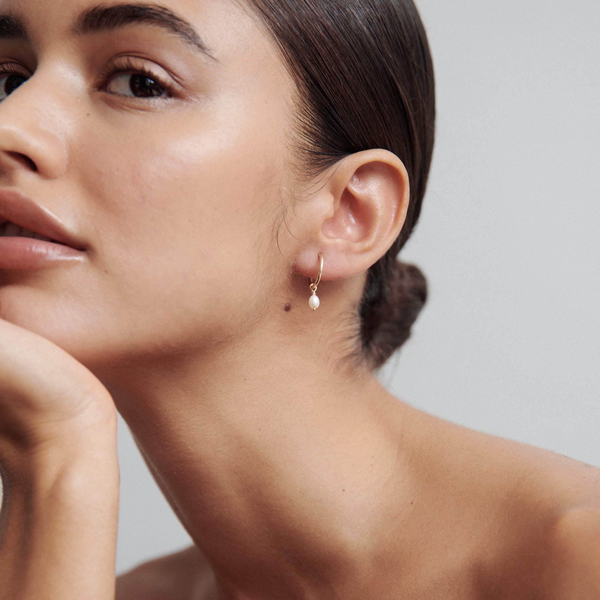 Woman wearing elegant gold hoop earring with a pearl drop, hair in sleek bun, showcasing natural beauty and luxury jewellery fashion.