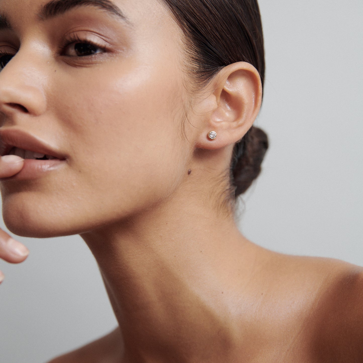 Woman showcasing a diamond stud earring, with smooth skin and sleek hair bun, representing luxury jewellery. Close-up, minimalist elegance.