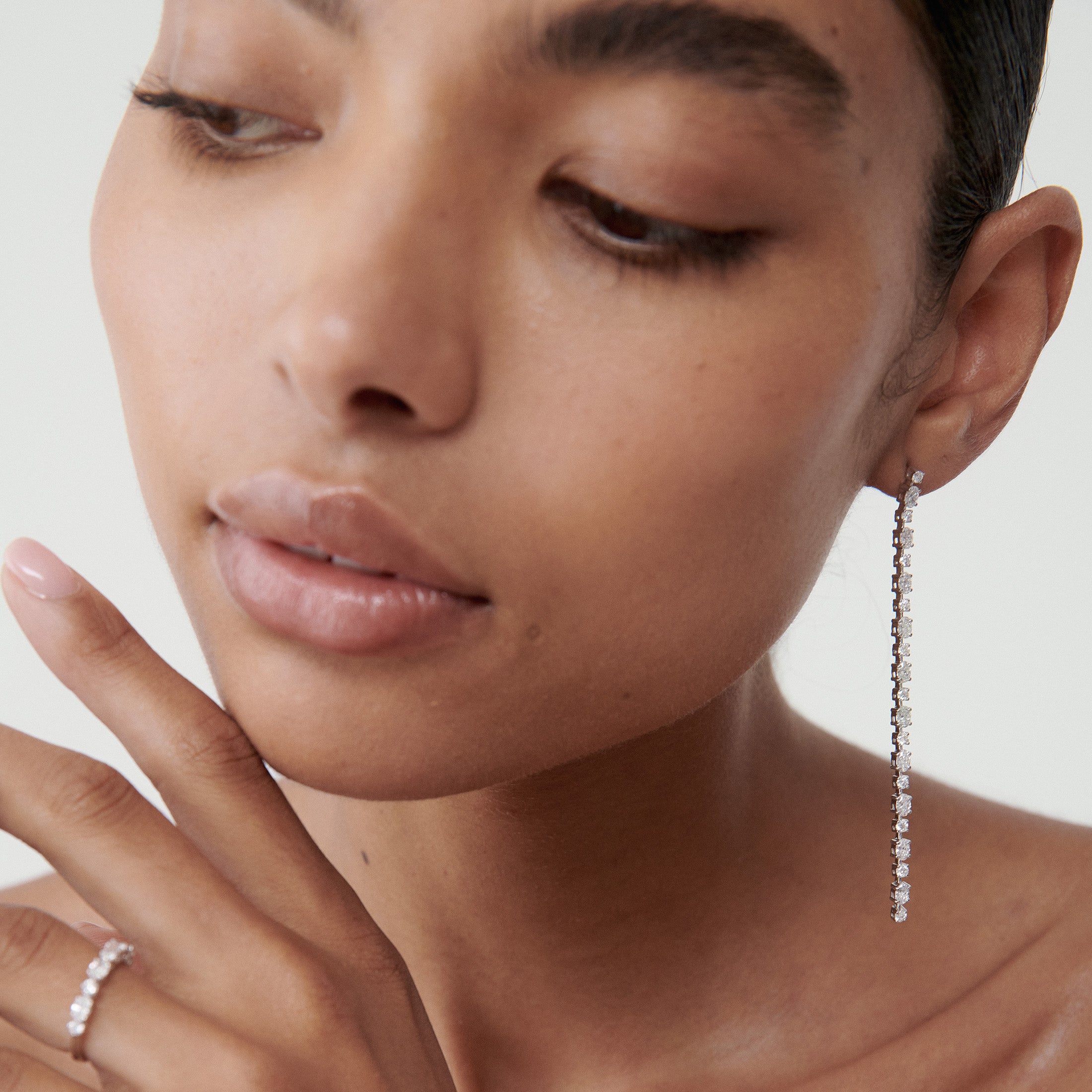 Elegant woman wearing long diamond drop earrings and a delicate ring. Close-up focuses on the luxurious jewellery's sparkle and design.