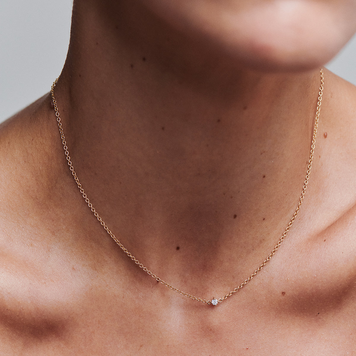 Close-up of a person wearing a delicate gold necklace with a small gemstone on a neutral background