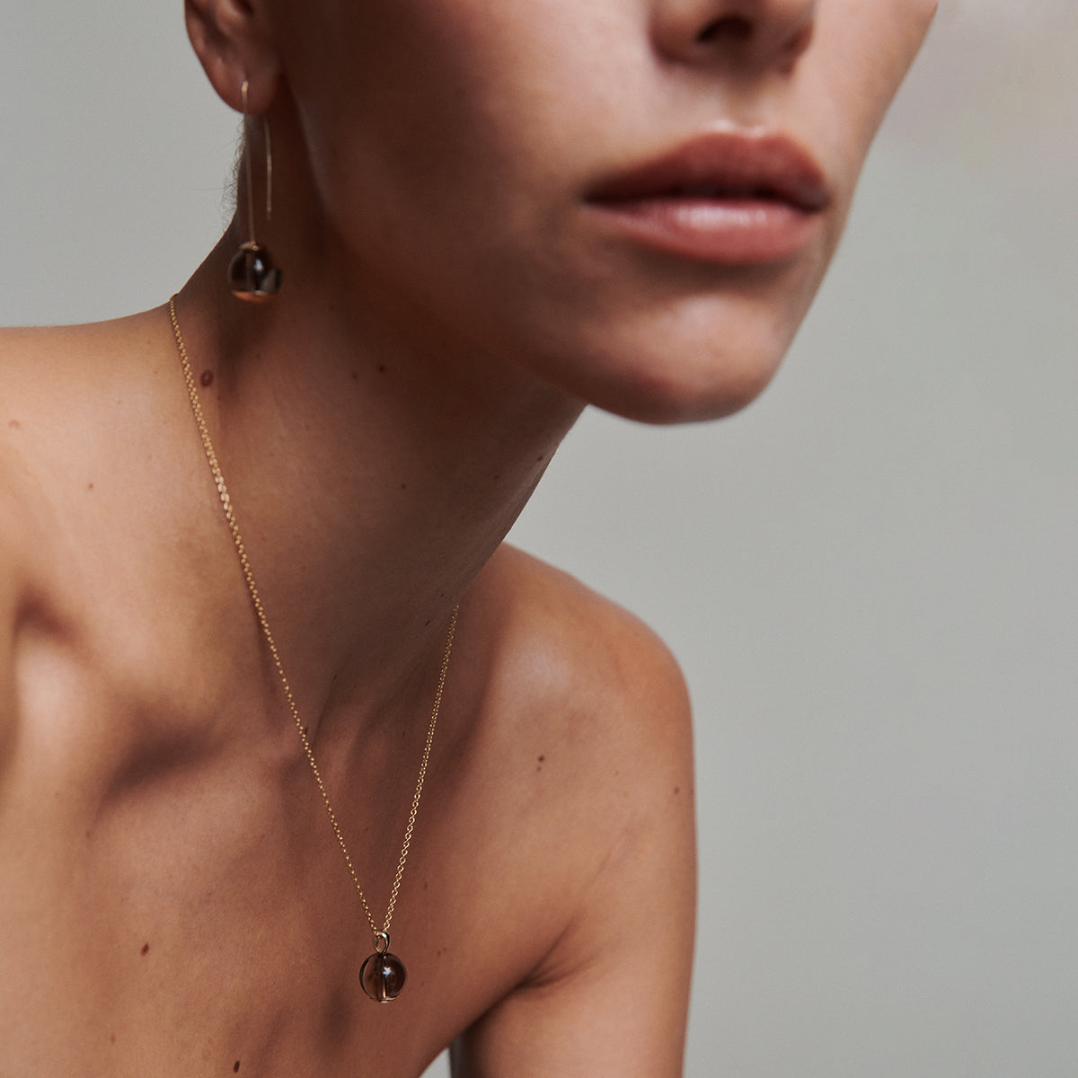 A close-up image of a person wearing a gold-toned necklace with a quartz pendant.
