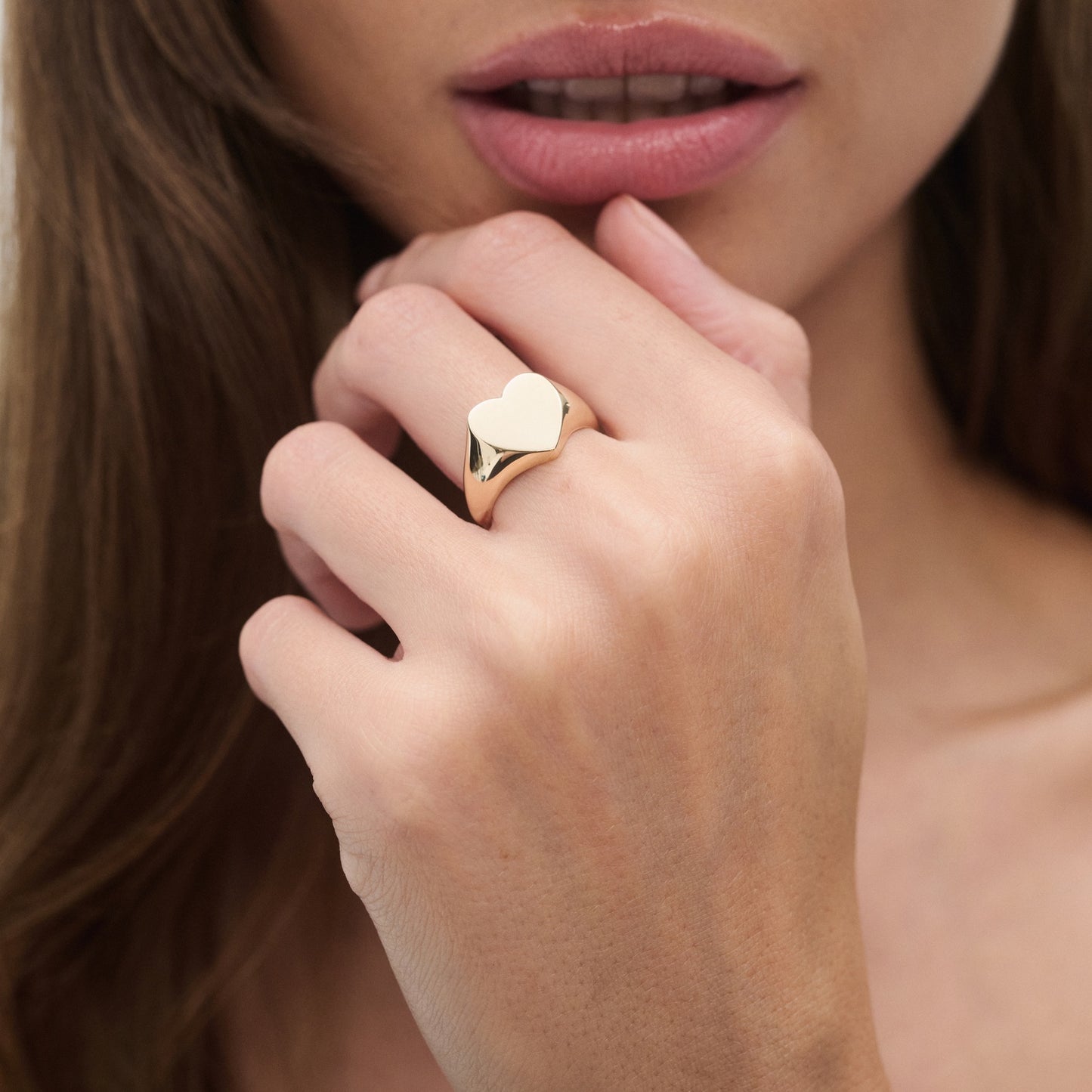 Close-up of a woman's hand wearing a gold heart-shaped signet ring, highlighting luxury jewellery and elegant style.
