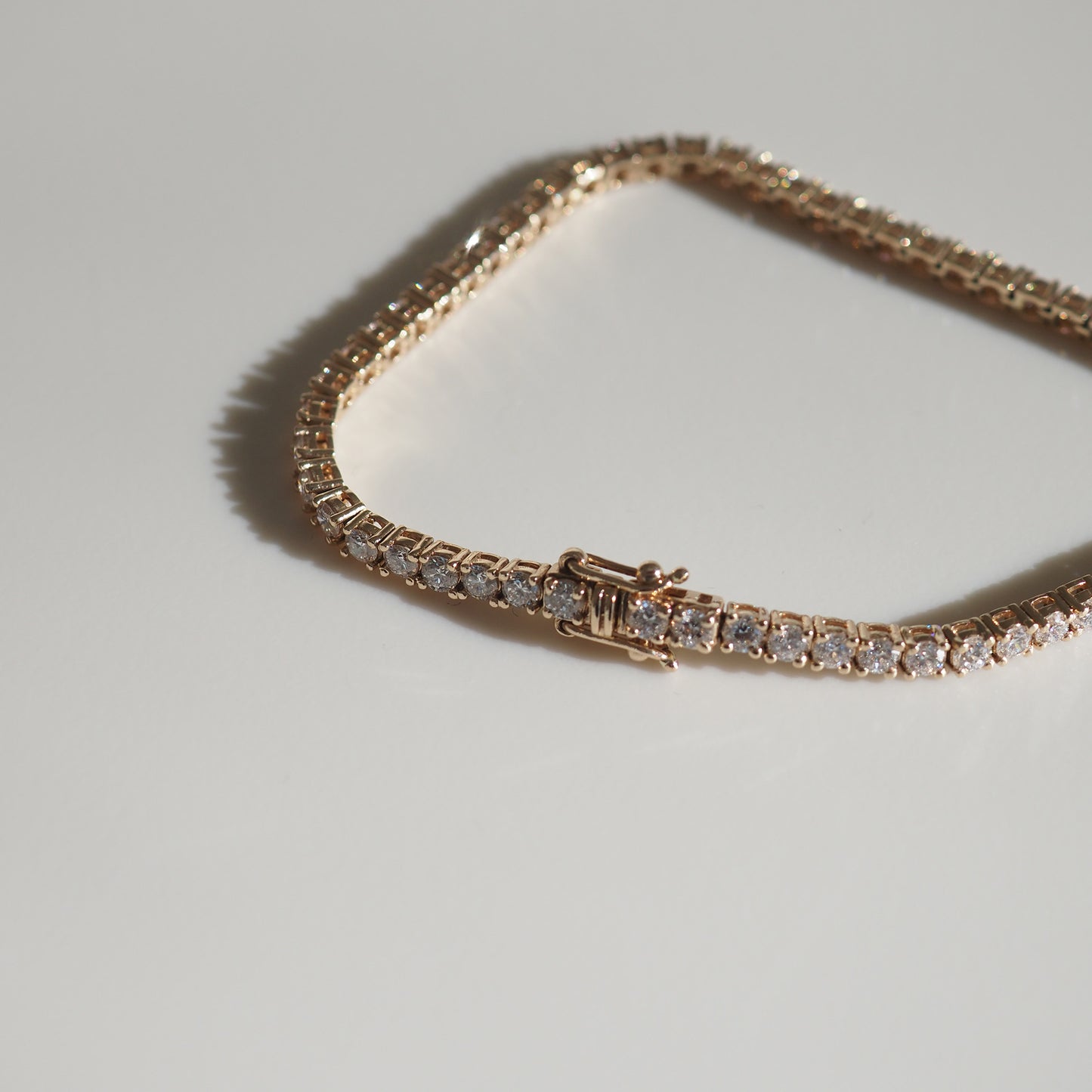 Elegant diamond tennis bracelet in gold with sleek clasp, displayed on a light surface, casting soft shadows. Perfect luxury jewellery piece.