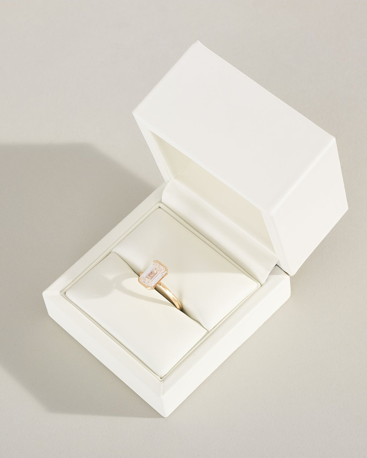 Gold ring with a pink gemstone in an open white jewelry box on a light gray background