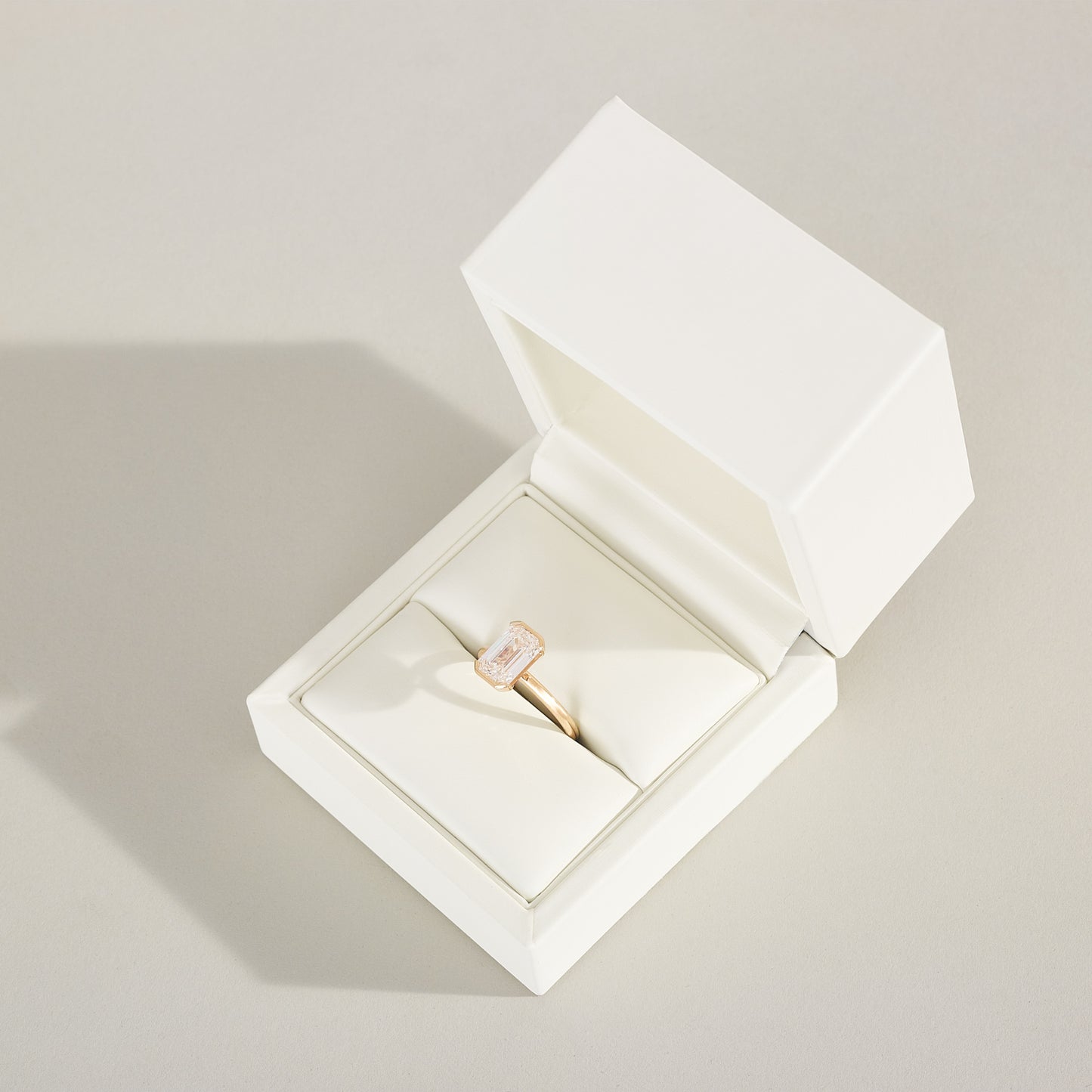 Gold ring with a pink gemstone in an open white jewelry box on a light gray background