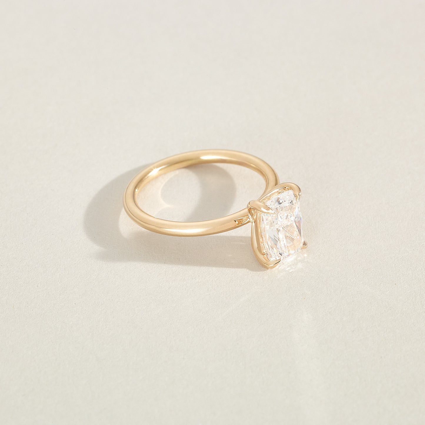 Gold ring with a cushion-shaped diamond on a light beige background