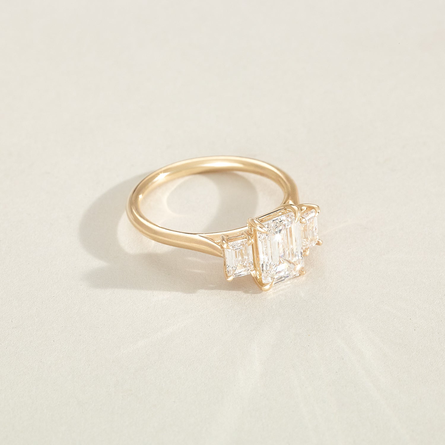 Gold ring with two emerald-cut diamonds on a light beige background