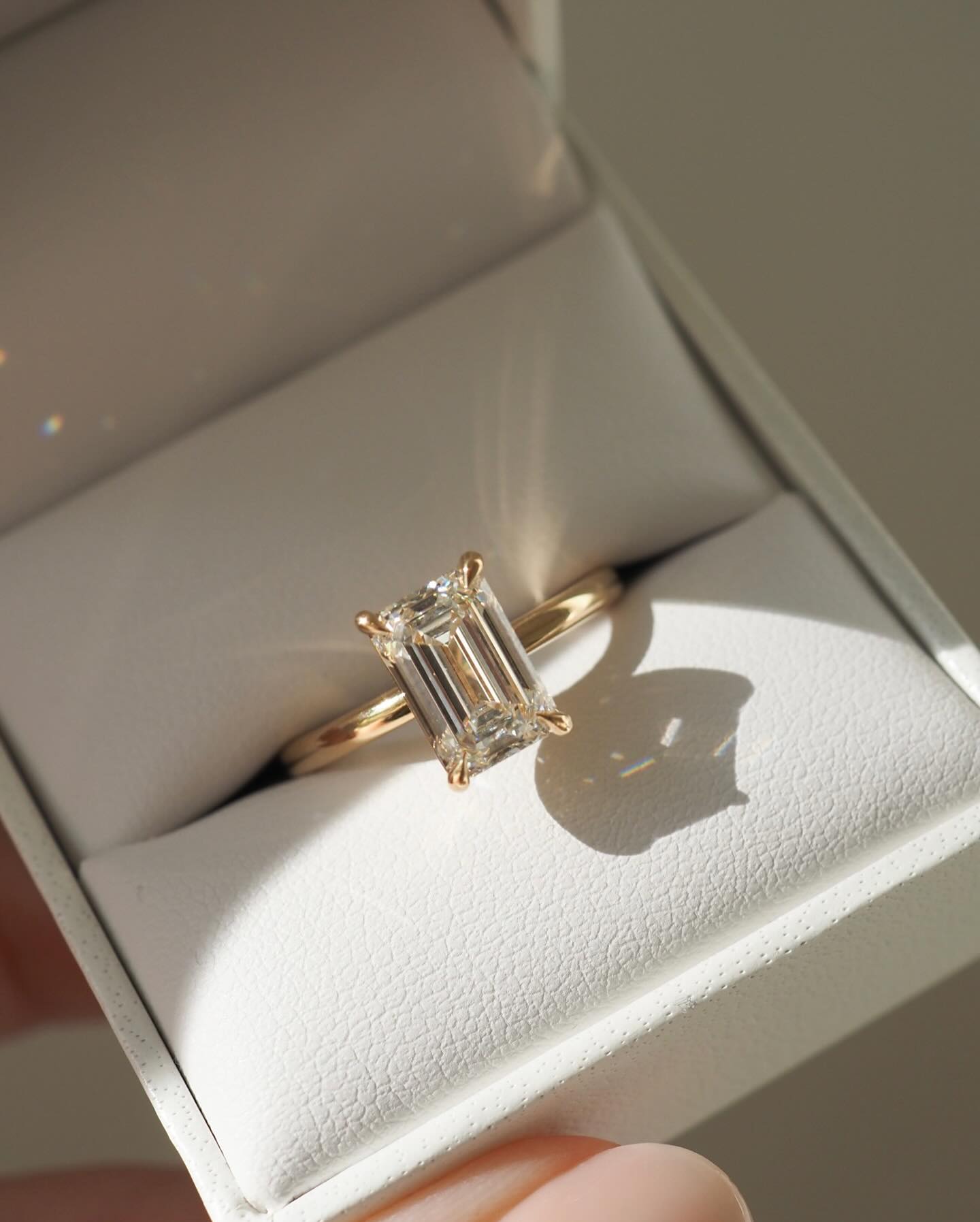 Emerald-cut diamond ring in a gold band, elegantly displayed in a white jewellery box, highlighting luxury and sophistication.