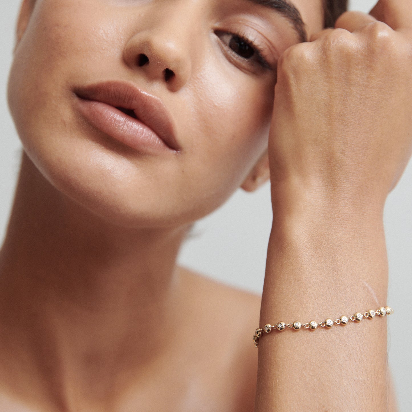 Woman wearing an elegant gold bracelet with intricate details, against a neutral background; luxury jewellery fashion.