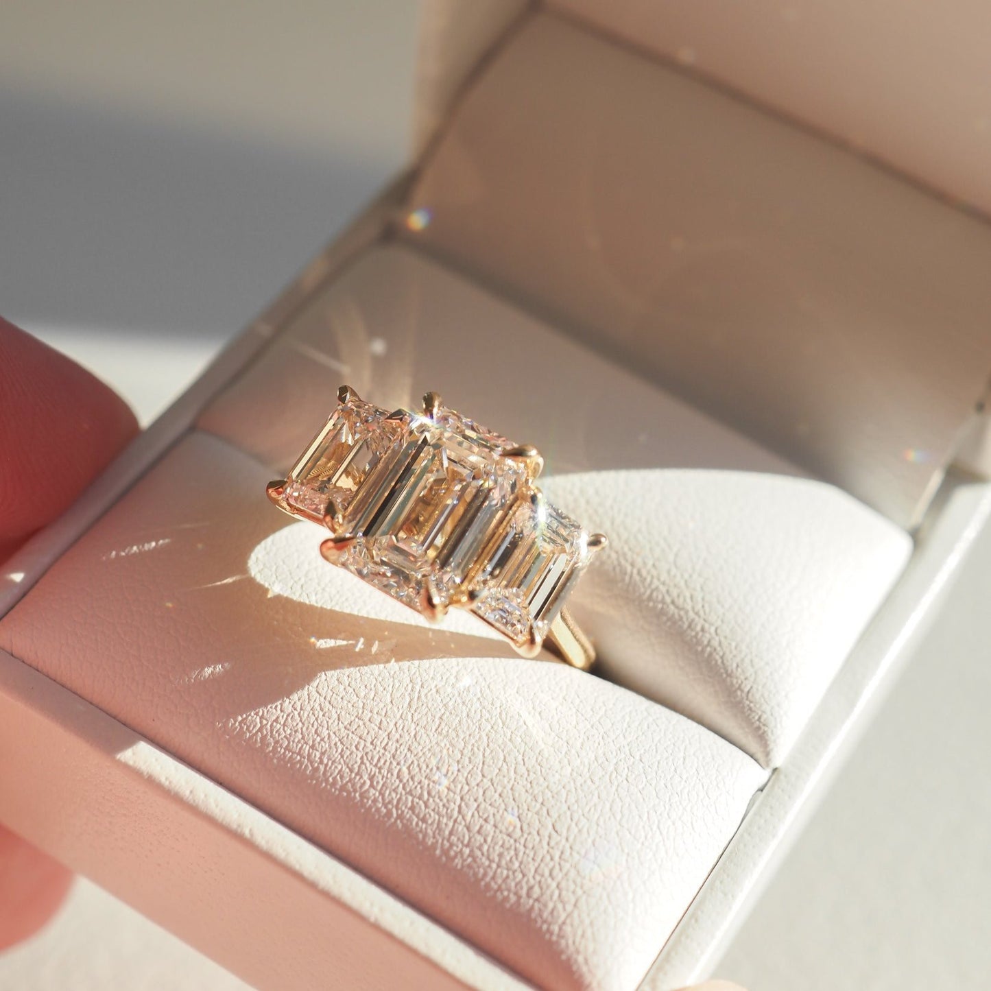 Elegant emerald-cut diamond ring displayed in a luxurious white box, capturing sunlight for a stunning sparkle. Perfect for high-end jewellery lovers.