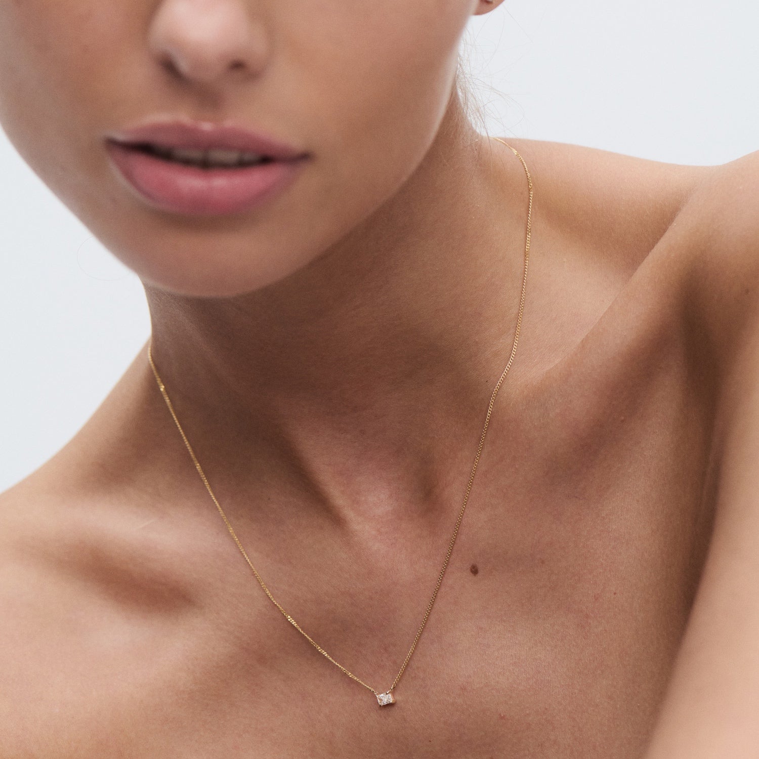 Close-up of a woman wearing an elegant gold necklace with a small diamond pendant. Ideal for luxury jewellery and fashion enthusiasts. [text overlay: Radiant] 