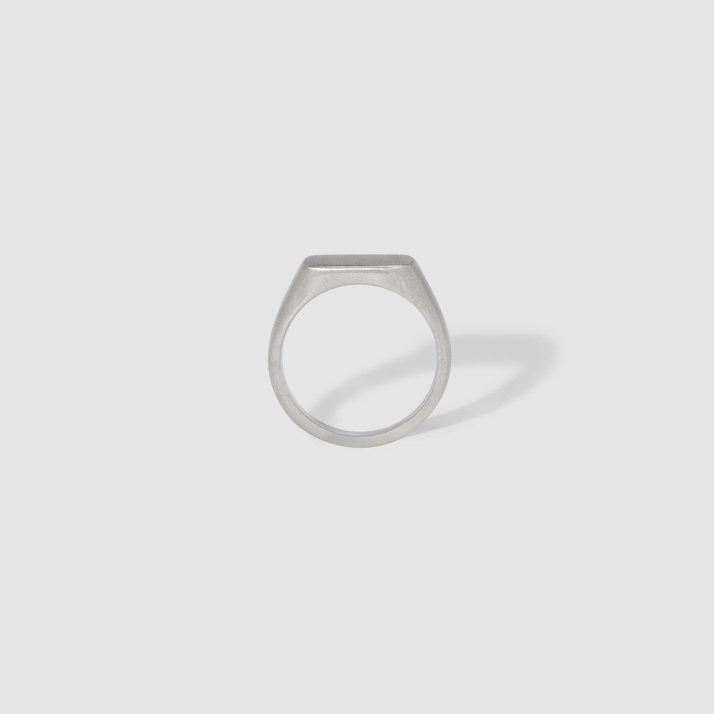Minimalist silver ring with a flat, rectangular face, displayed against a plain grey background. Modern luxury jewellery piece.