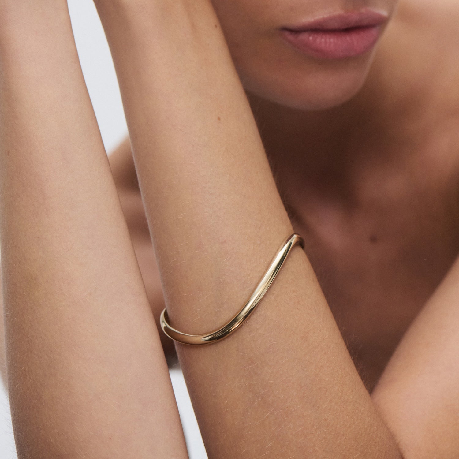 Elegant gold bangle on woman's wrist, highlighting luxury jewellery fashion with minimalist design. [text overlay: Medium] [text colour: #000000]
