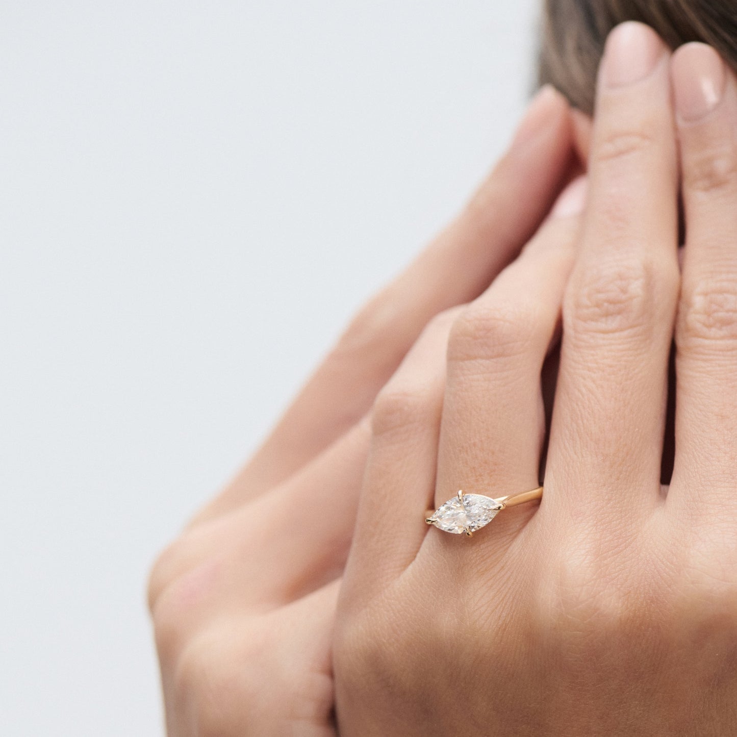 A woman's hand with a marquise-cut diamond ring set in yellow gold, shown against a blurred background, epitomising luxury jewellery style.