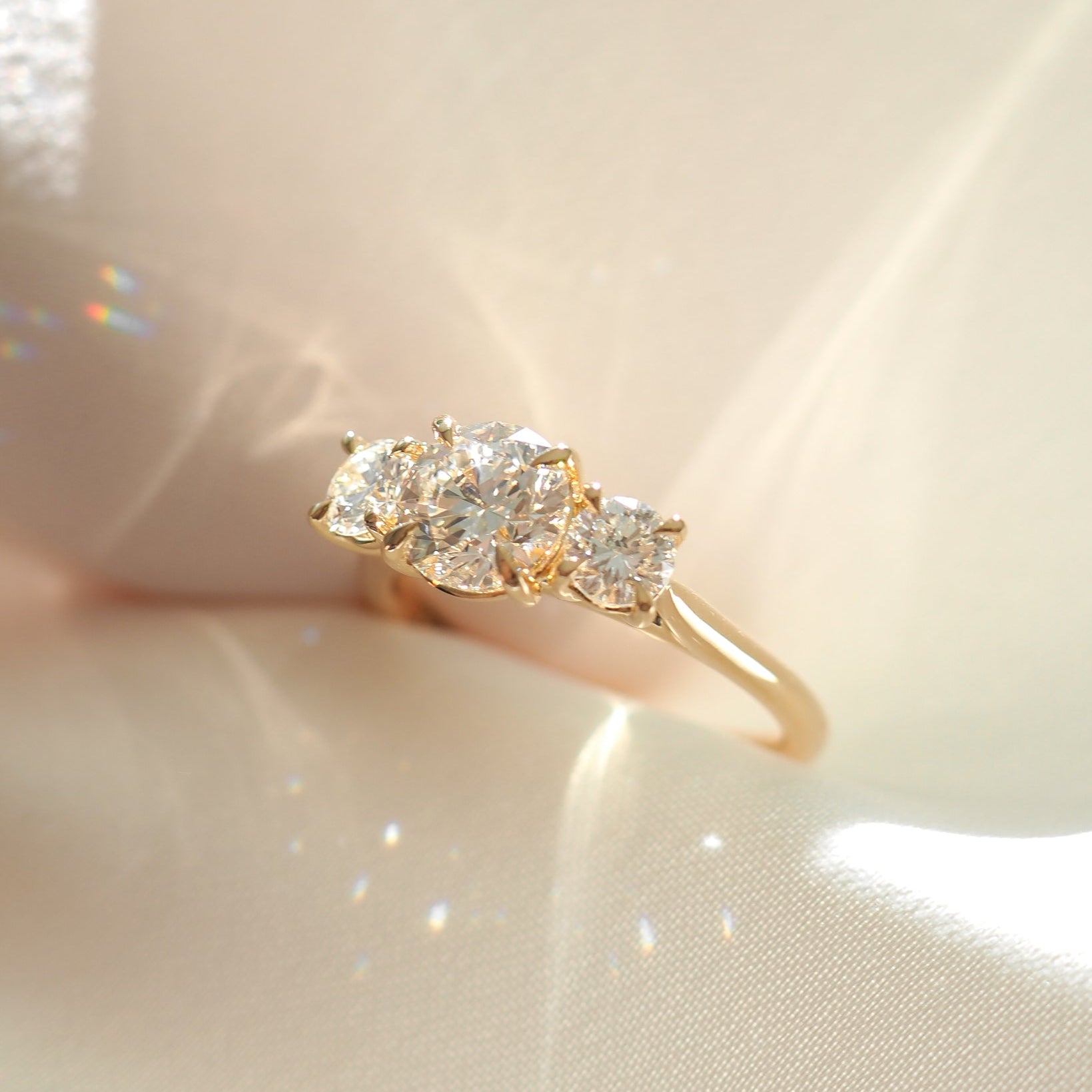 Elegant gold ring with three sparkling diamonds, displayed on soft satin fabric with subtle light reflections. Perfect for luxury jewellery lovers.