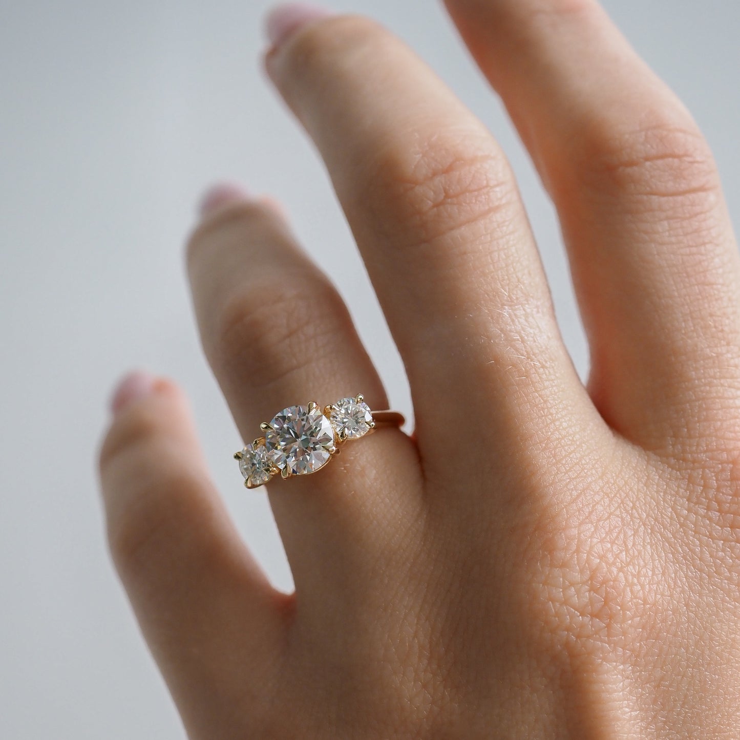 A hand wearing a round lab-grown diamond engagement ring with a Trilogy design.