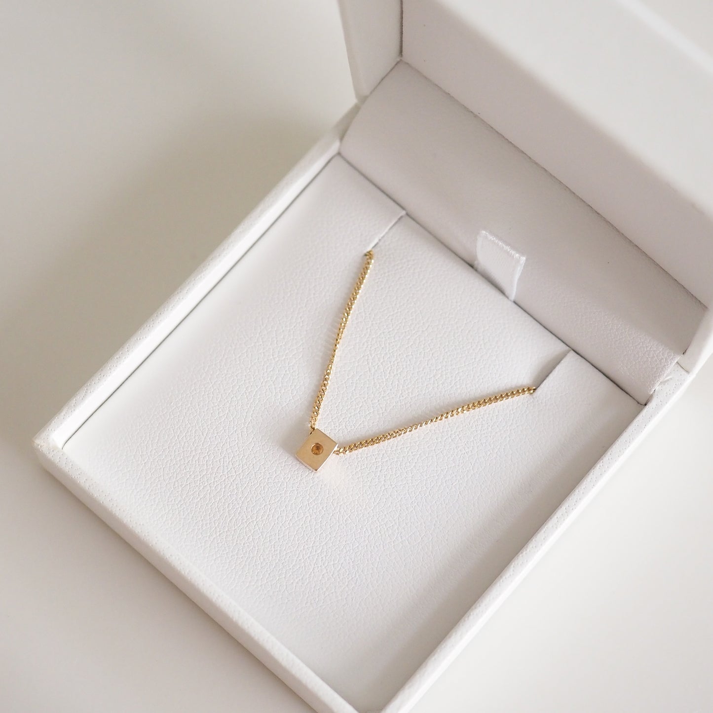 Gold chain necklace with a small square pendant, elegantly presented in a white jewellery box. Perfect for luxury fashion lovers.