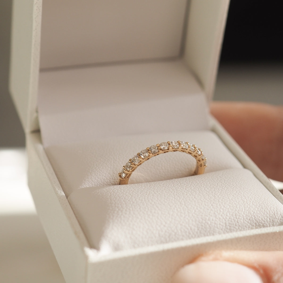 Gold eternity ring with diamonds in a white jewellery box. Hand seen holding the box, showcasing luxury and elegance.