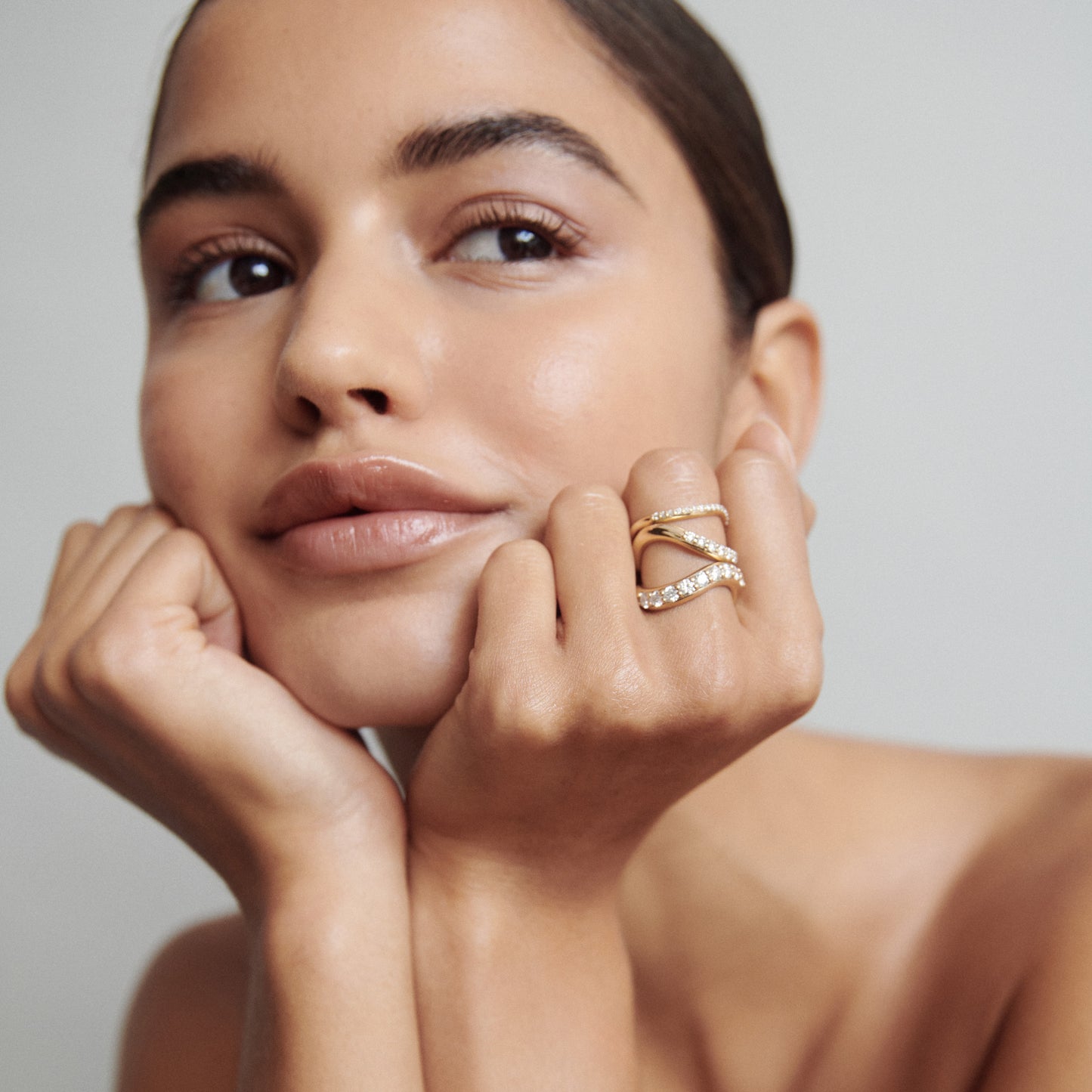 Woman with a serene expression wearing a gold and diamond criss-cross ring, resting her chin on her hands against a light grey background. [text overlay: Fine (top), Medium (middle) and Bold (bottom)] 