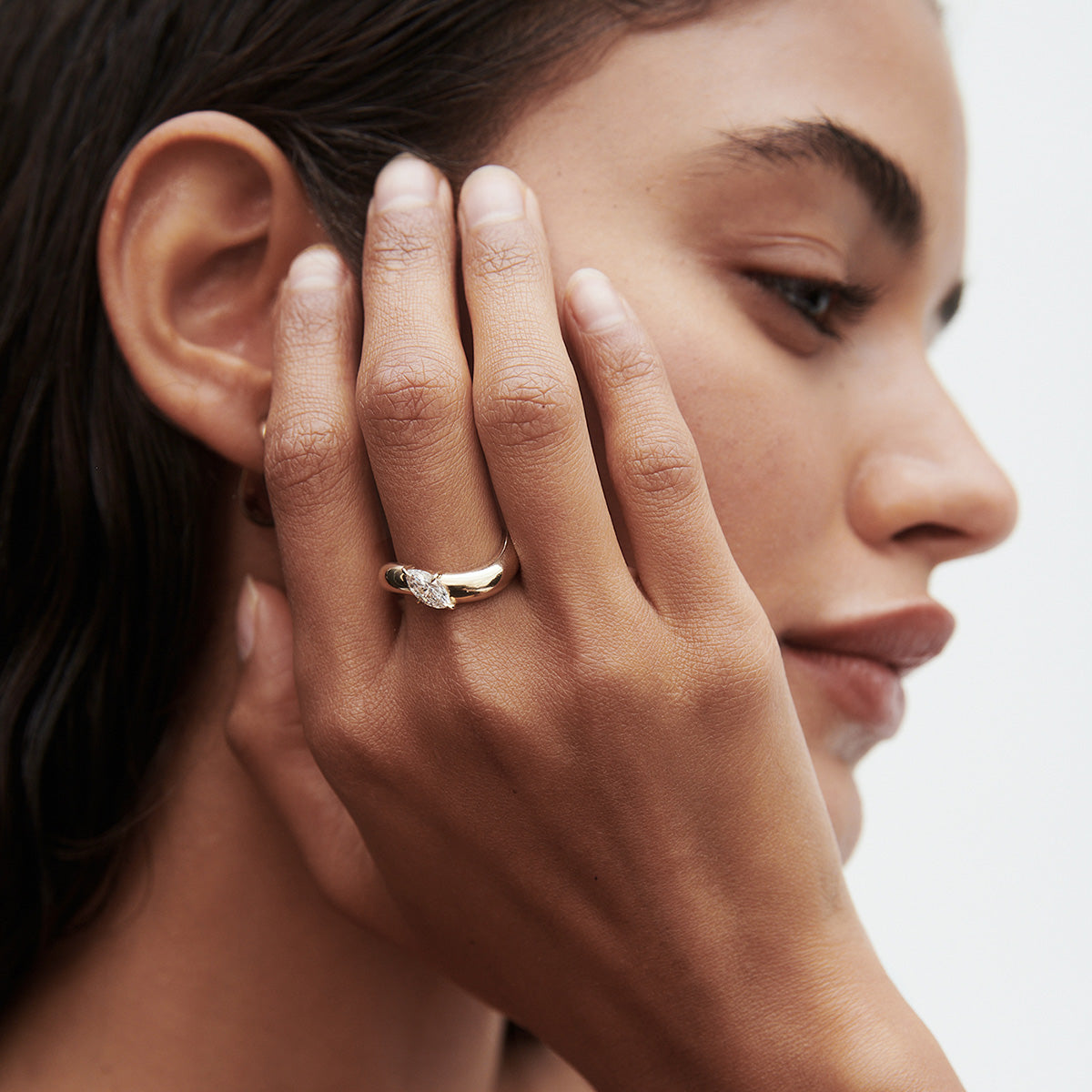 Woman with gold diamond ring, gently touching her face. Close-up profile shot showcasing luxury jewellery elegance.