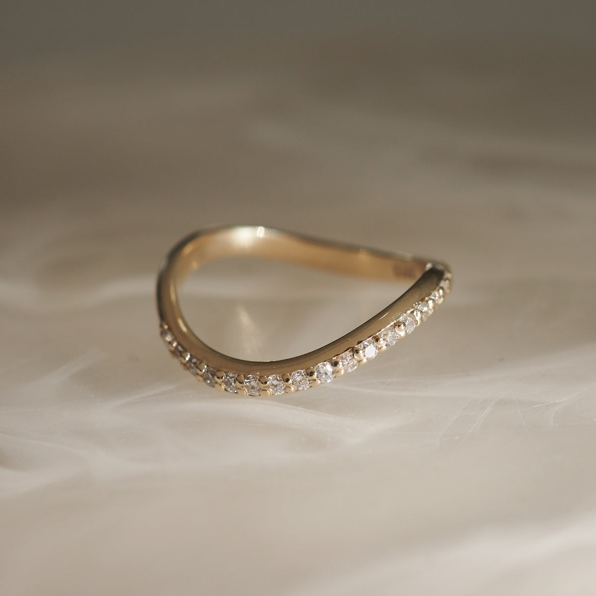 Gold chevron ring with a row of sparkling diamonds on a marble surface, embodying luxury jewellery elegance.