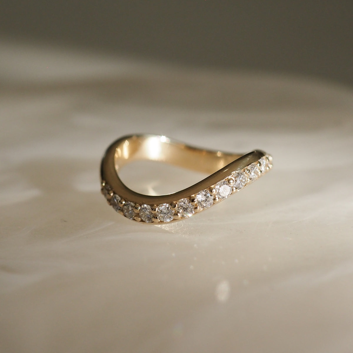 Elegant gold ring with a modern, curved design, adorned with sparkling diamonds, set on a softly lit, smooth surface. Perfect for luxury jewellery.