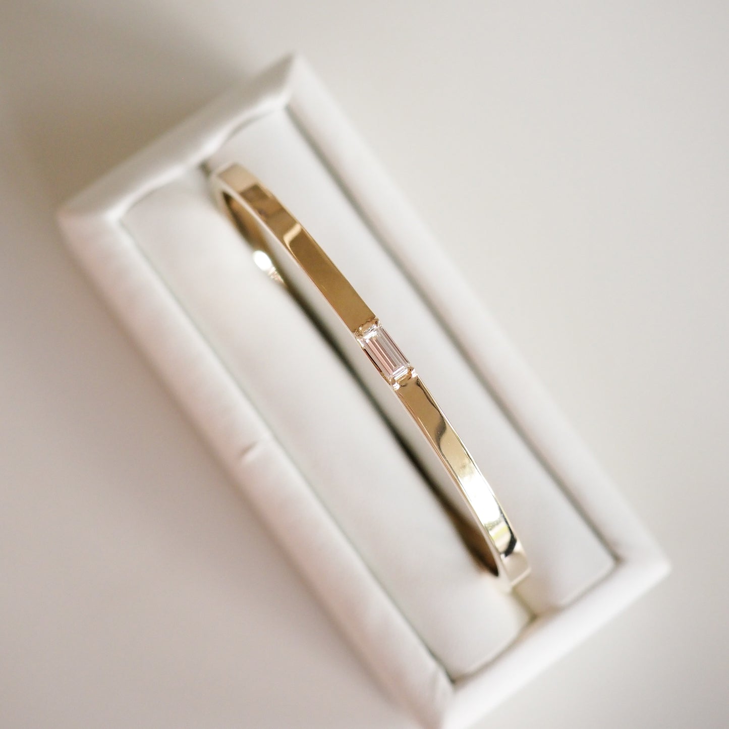 Gold bracelet with baguette-cut diamond centrepiece, set in a white jewellery box. Elegant, luxury accessory for special occasions.