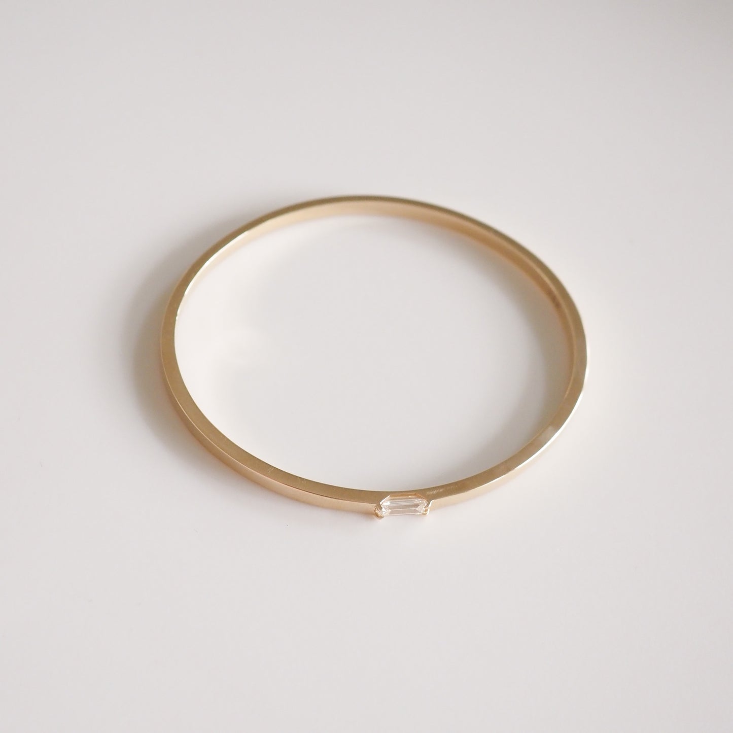 Gold bangle with minimalist design, featuring a sleek, round shape and a subtle, elegant clasp. Luxury jewellery piece on white background.