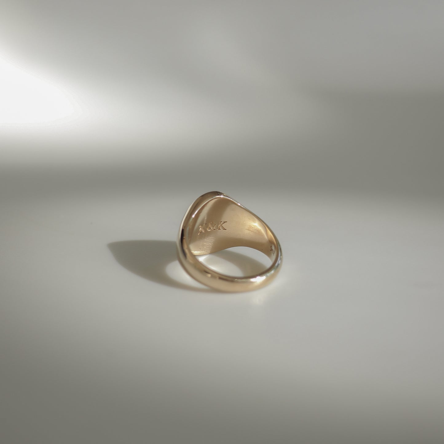 Gold ring with a smooth, rounded design on a soft, light background. The inside displays engraved initials "A&R", suggesting bespoke craftsmanship.