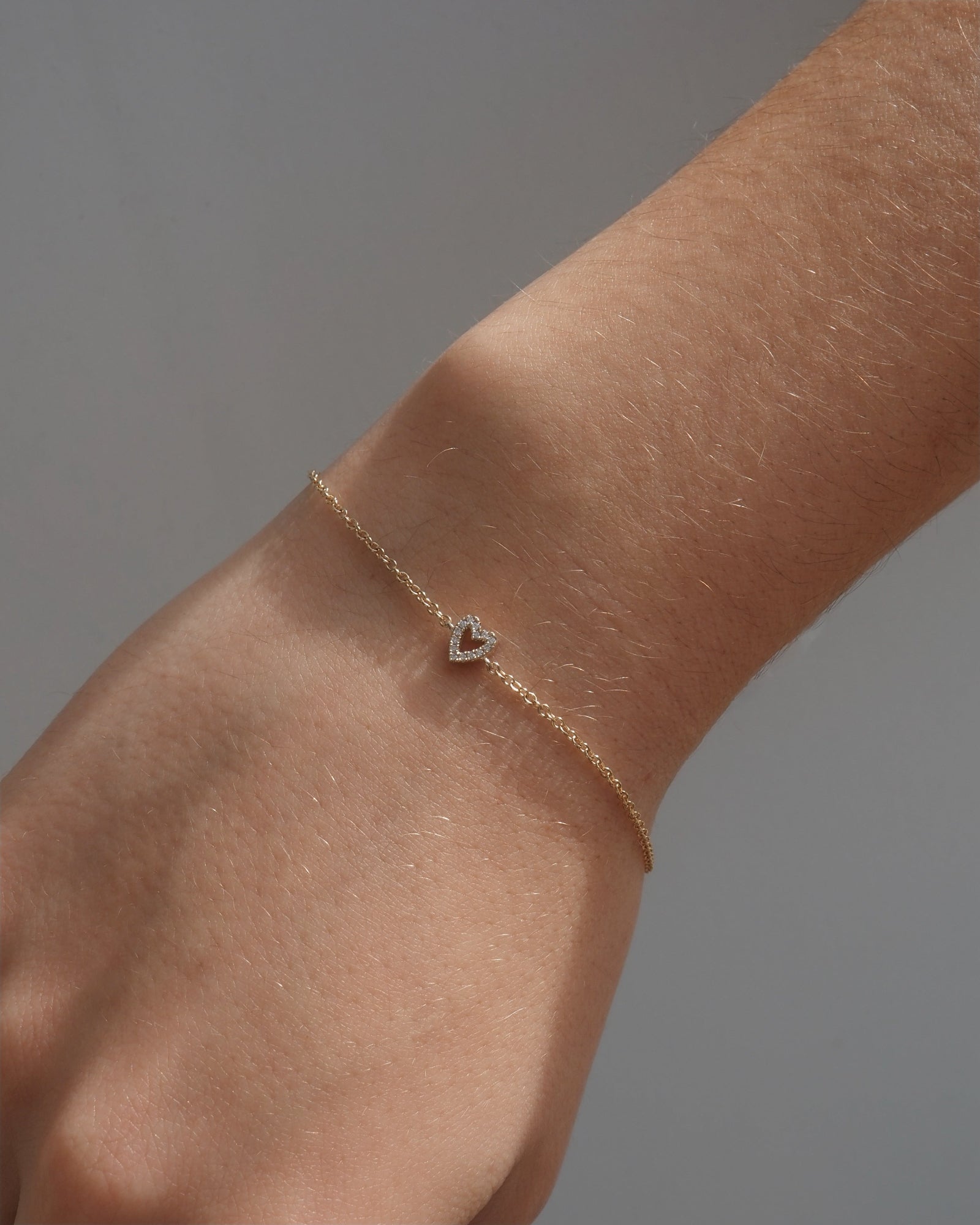 A delicate gold chain bracelet with small lab grown diamonds, shown worn on a person's wrist against a neutral gray background.
