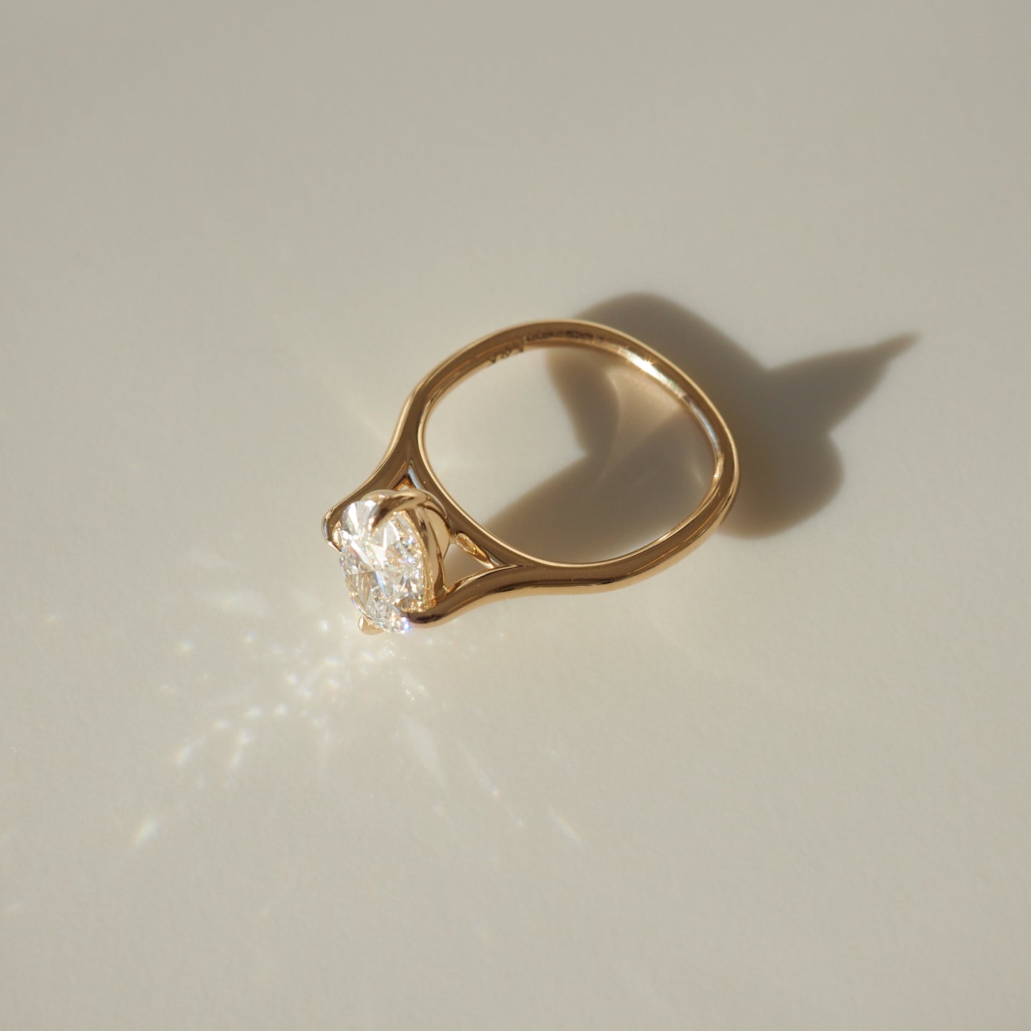 Gold ring with a solitaire diamond reflecting light on a neutral surface. Luxurious and elegant jewellery design.
