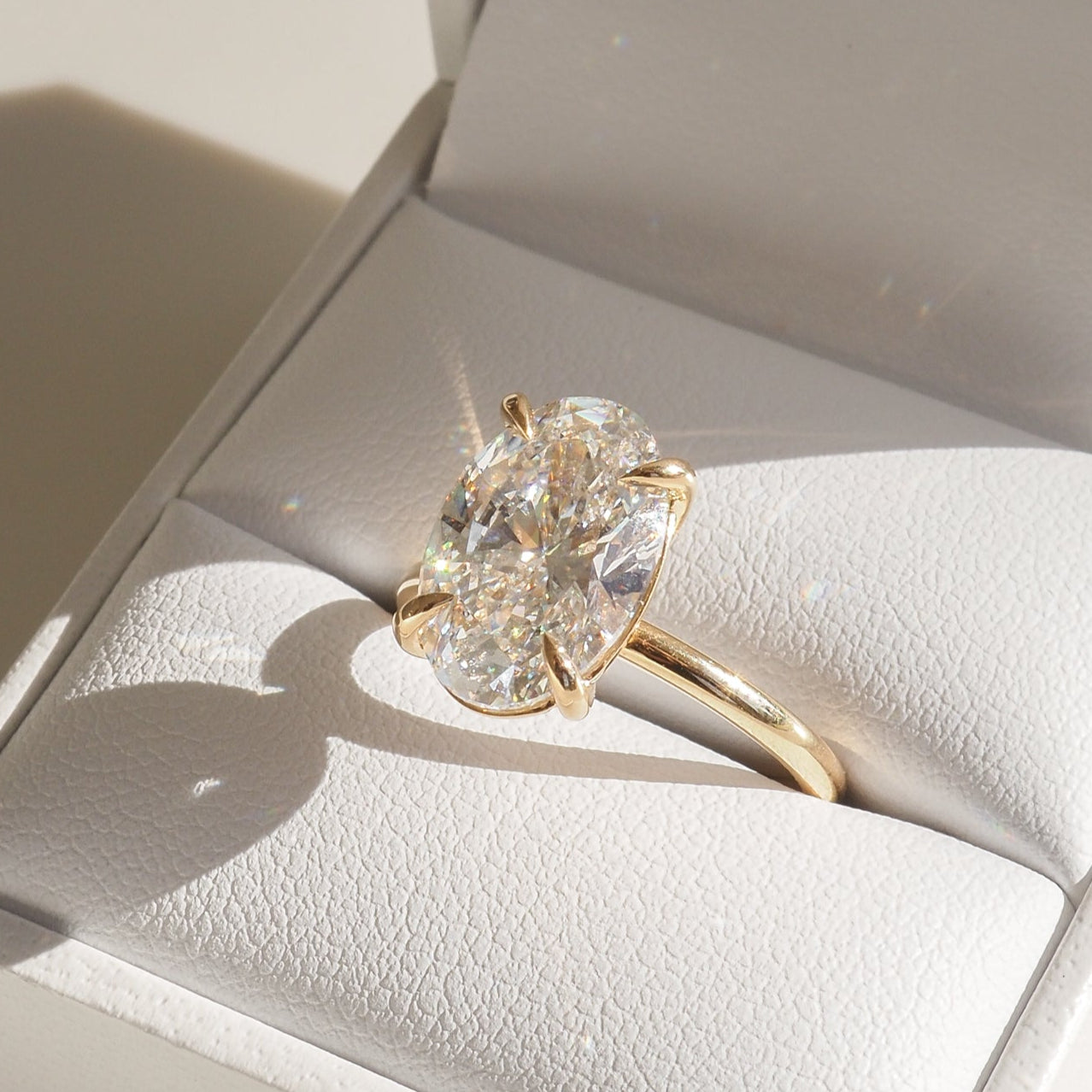Gold ring with a large, sparkling oval diamond displayed in an open white jewellery box, featuring the brand "Kate & Kole".