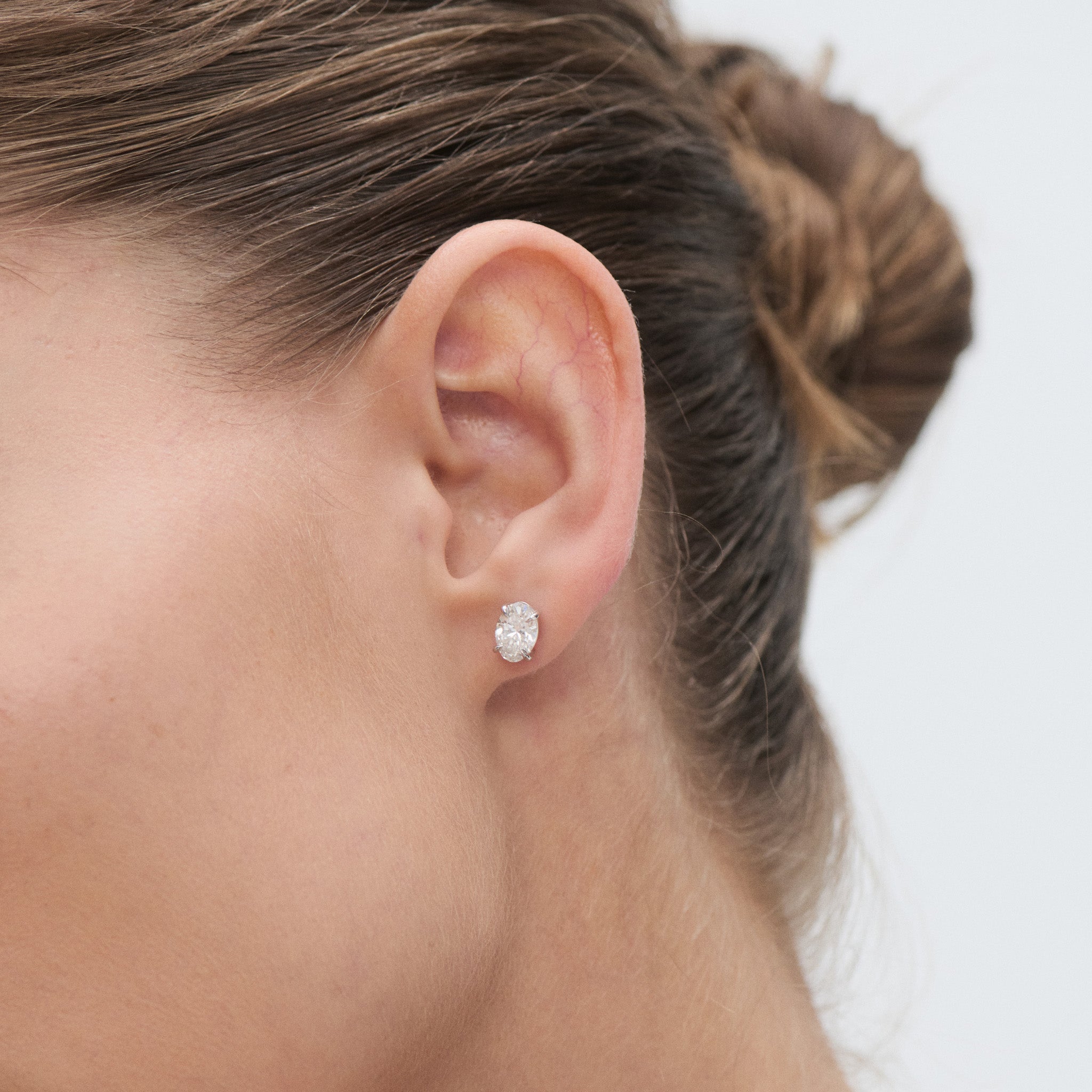 Close-up of a model wearing an oval diamond earring with a blurred background