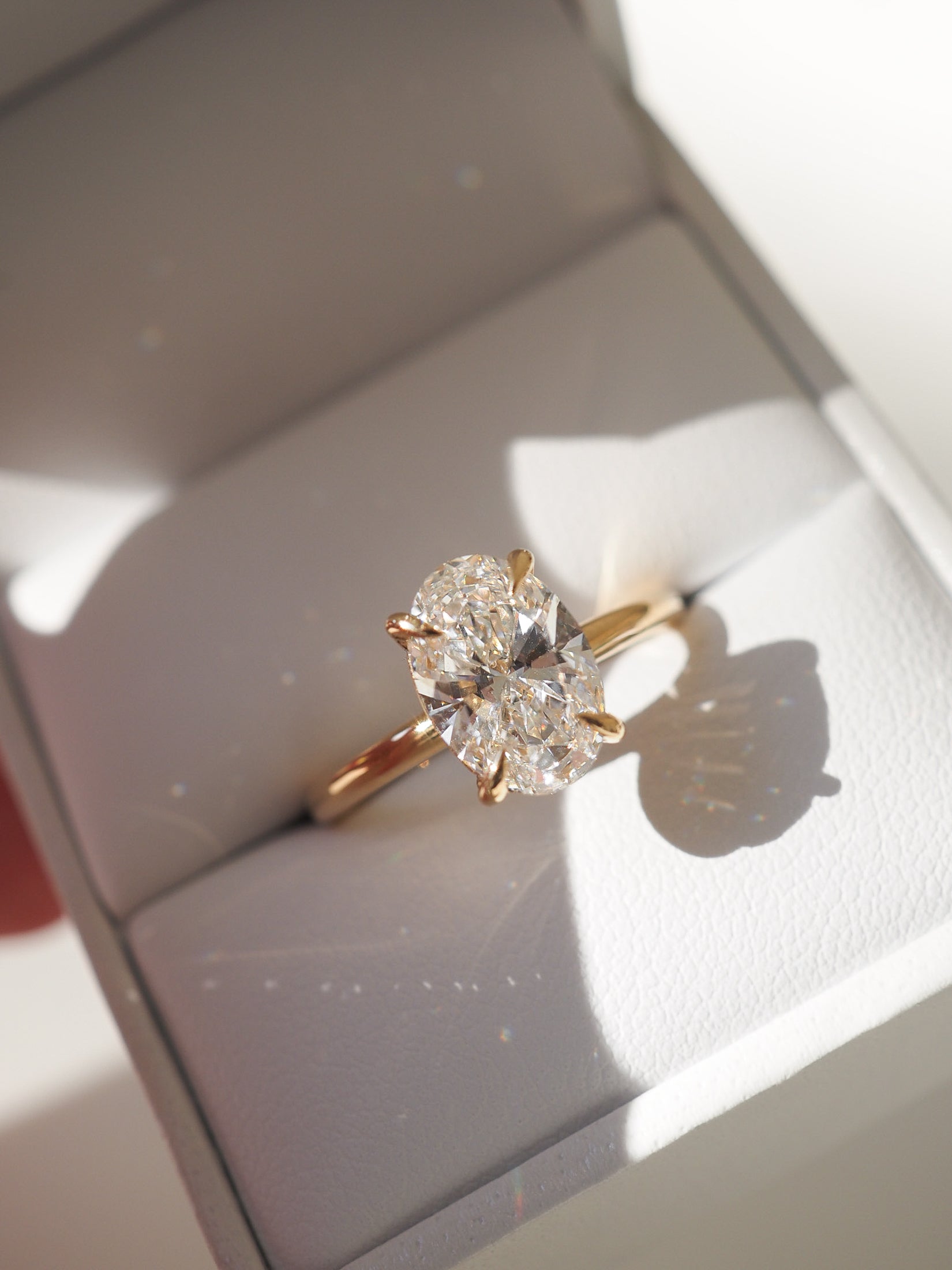 Elegant oval diamond ring with a gold band displayed in a white jewellery box, capturing the essence of luxury.