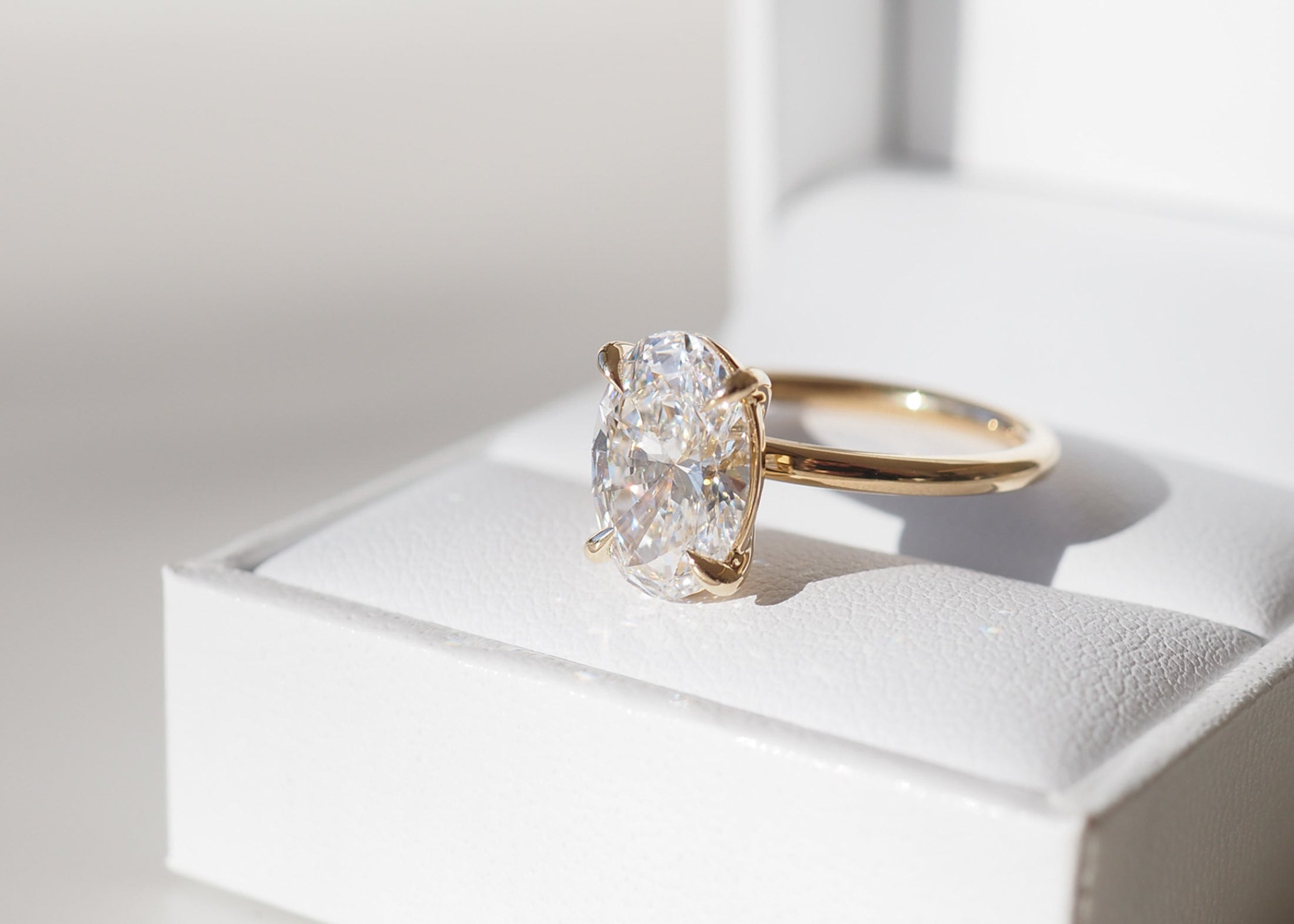 Gold ring with an oval diamond in a jewellery box, sparkling in bright light. Luxurious design ideal for engagements or special occasions.