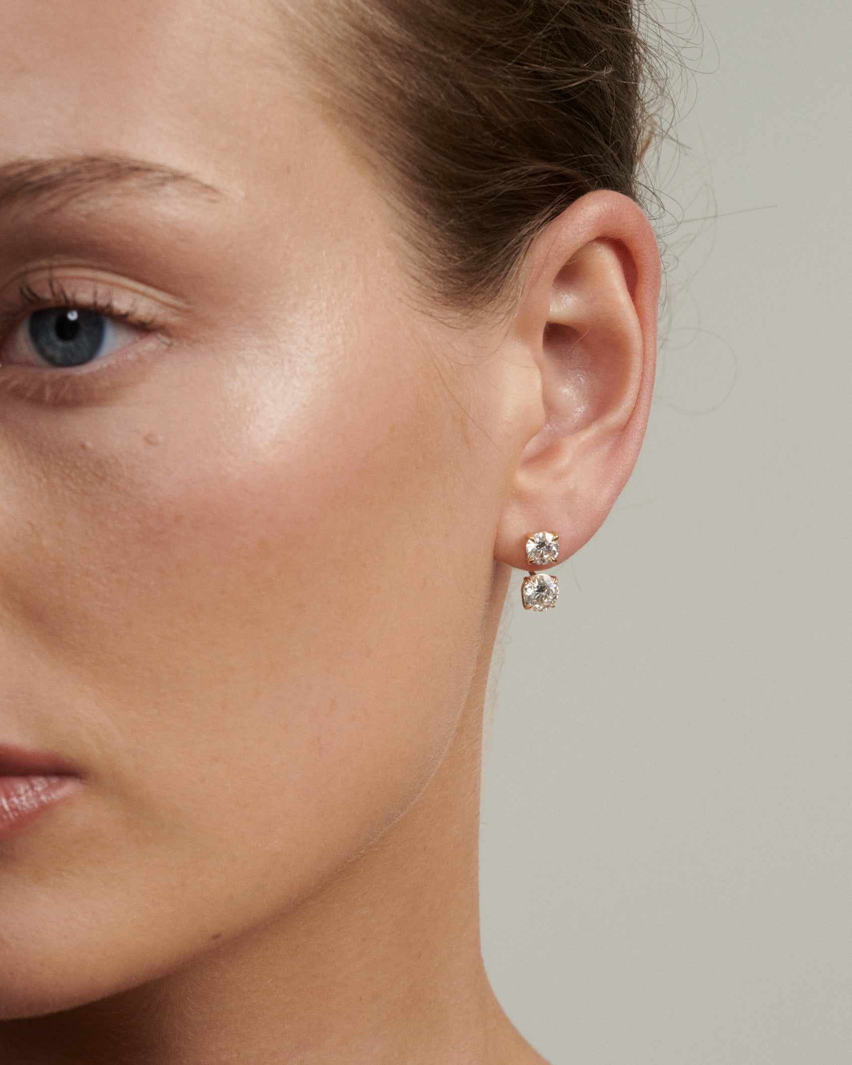 Close-up of a woman wearing diamond earrings with a neutral background