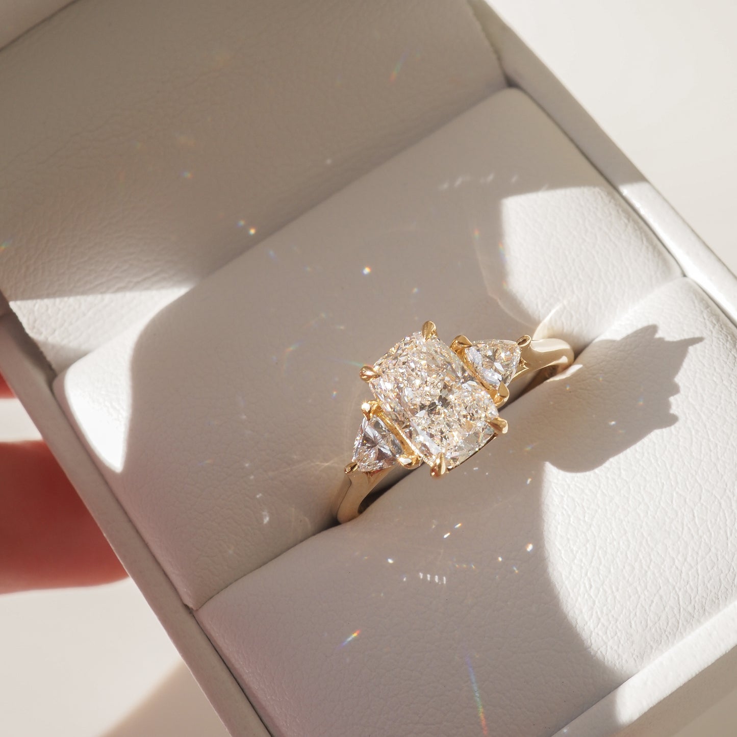 Luxury gold ring with a radiant-cut centre diamond and two side stones in an elegant box. Perfect for elegant engagements or anniversary gifts.