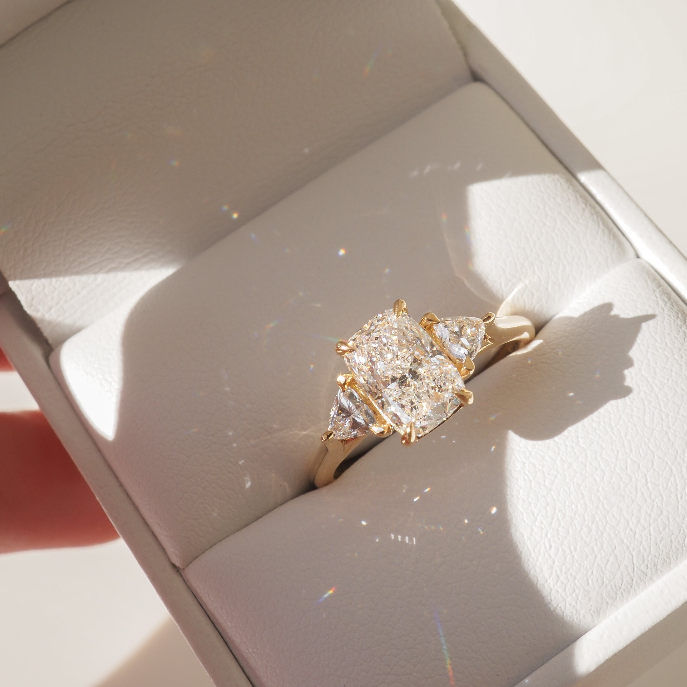 Luxury gold ring with a radiant-cut centre diamond and two side stones in an elegant box. Perfect for elegant engagements or anniversary gifts.
