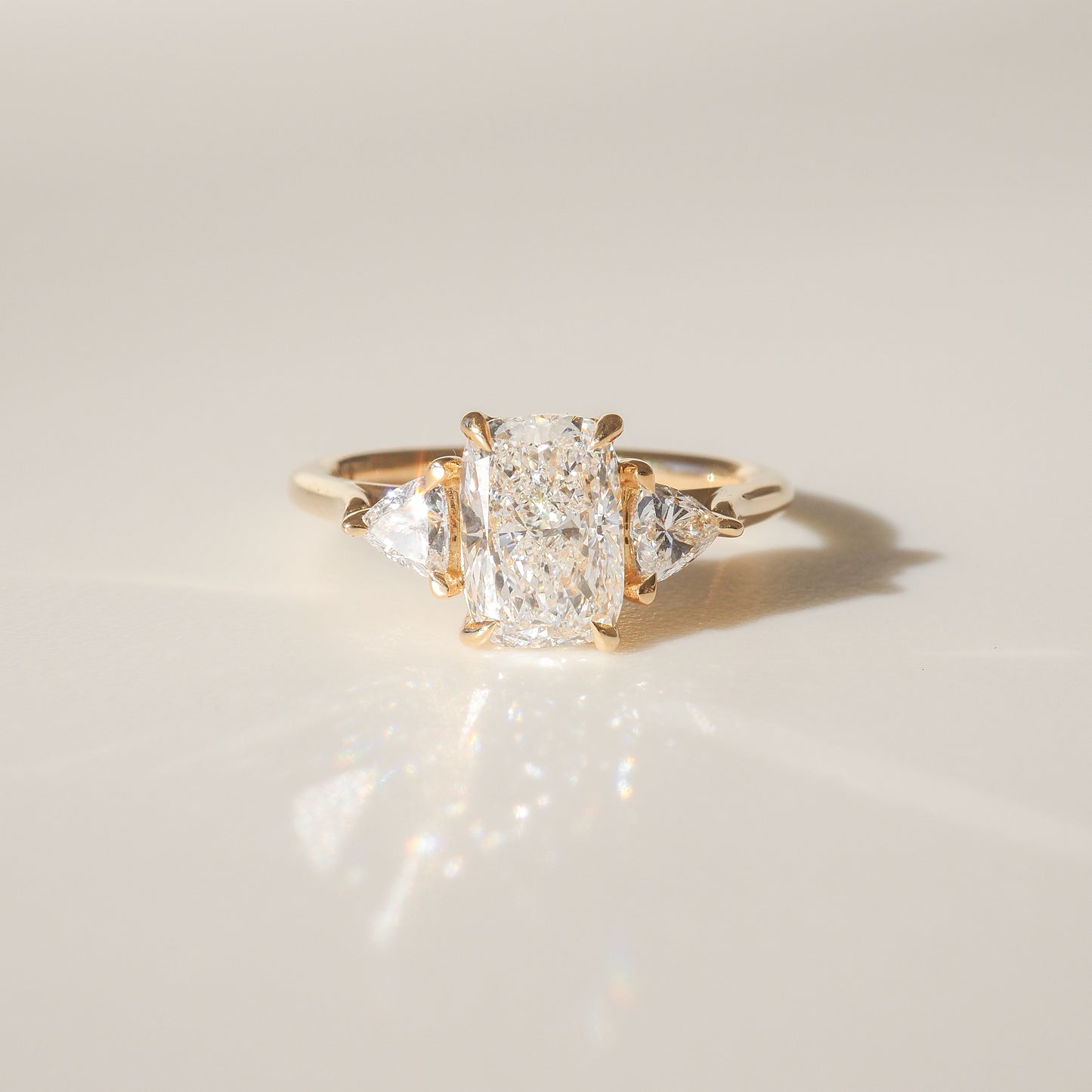 Gold ring with a central rectangular diamond flanked by two triangular diamonds, elegantly set against a soft, neutral background. Luxurious jewellery.