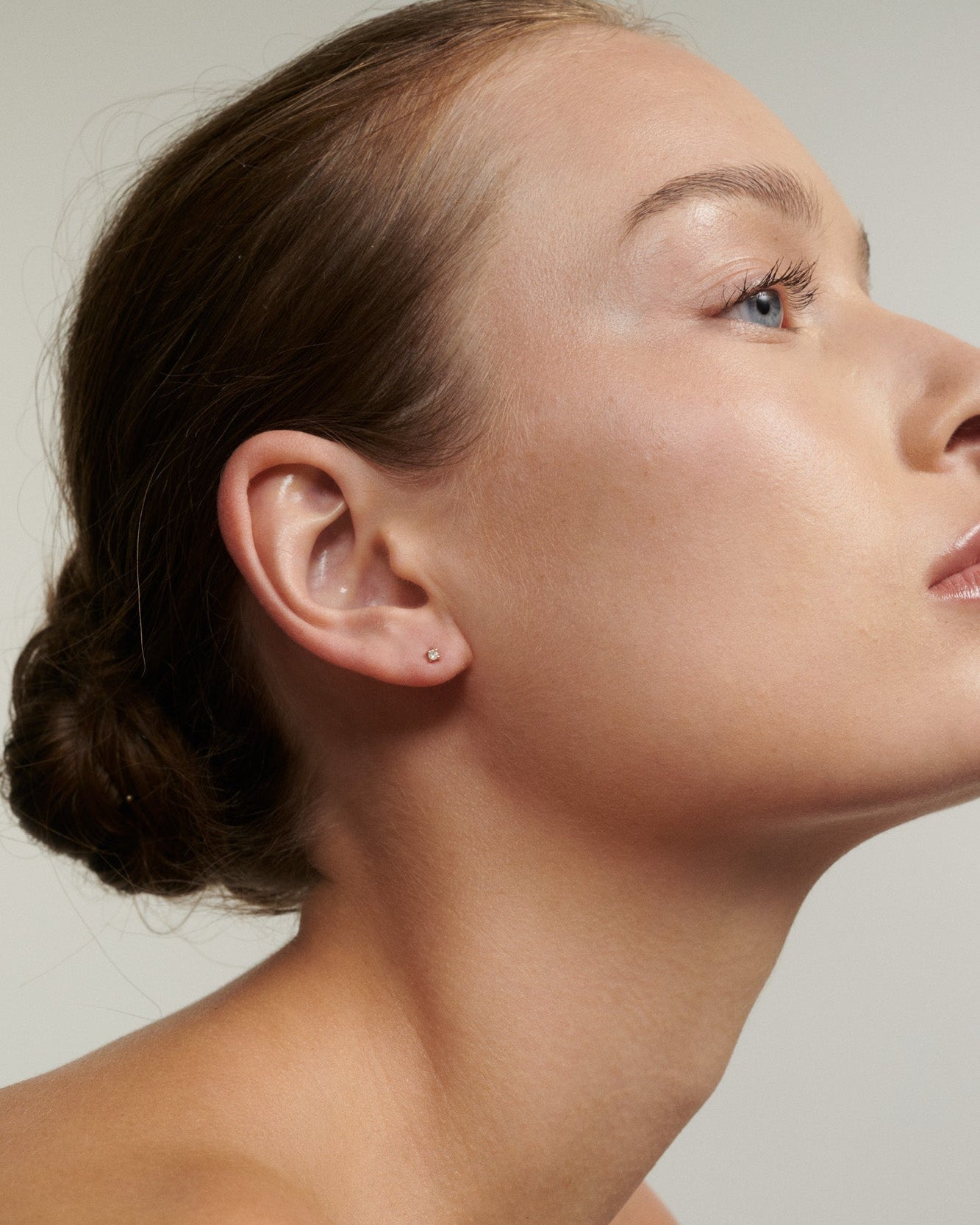 Close-up of a woman's ear with a small earring against a neutral background [text overlay: Lab-Grown Diamond]