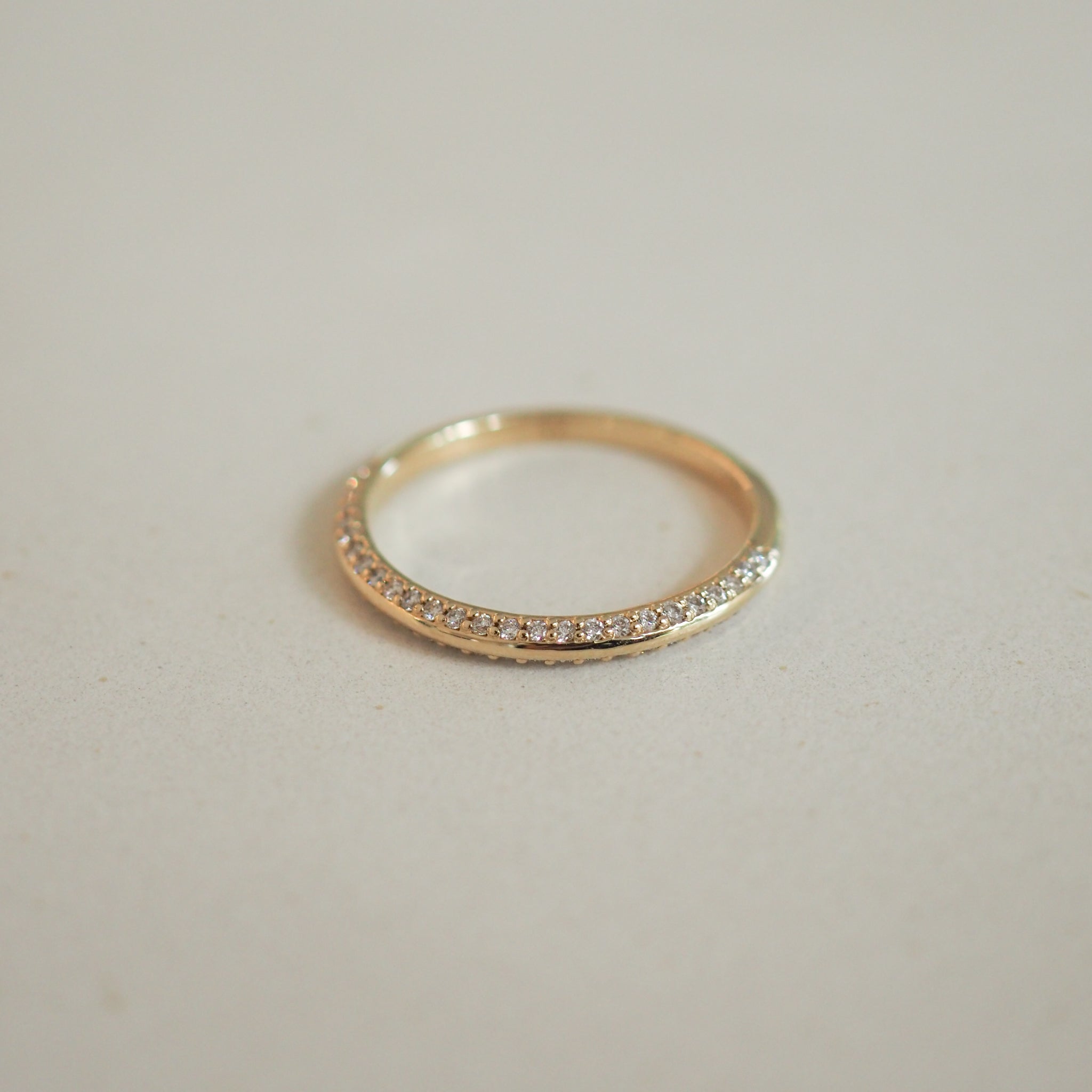 Elegant gold ring with a half-eternity band of sparkling diamonds, showcasing luxury jewellery craftsmanship on a neutral background.