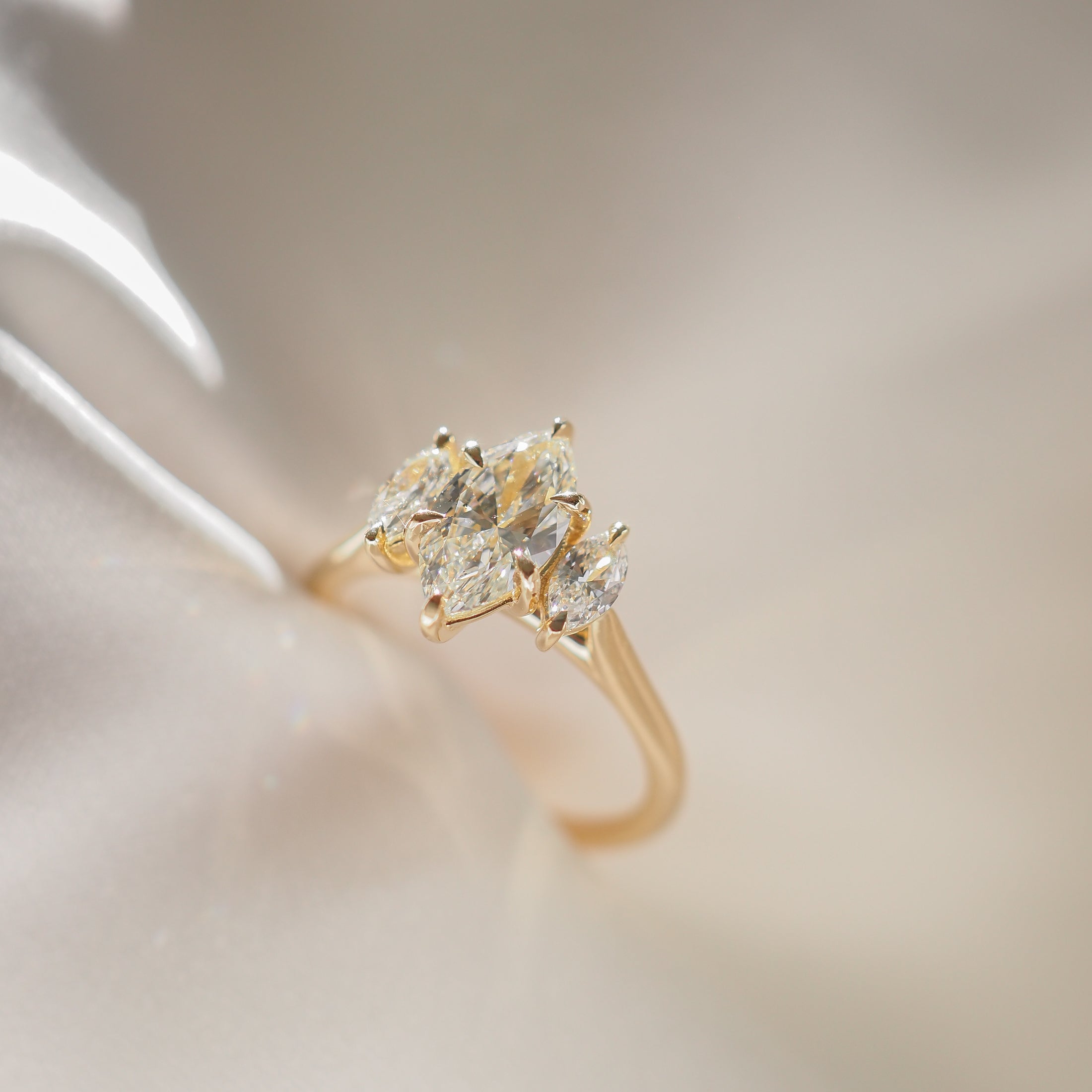 Elegant gold ring with three marquise-cut diamonds on a soft, shimmering background. Ideal for luxury jewellery enthusiasts.