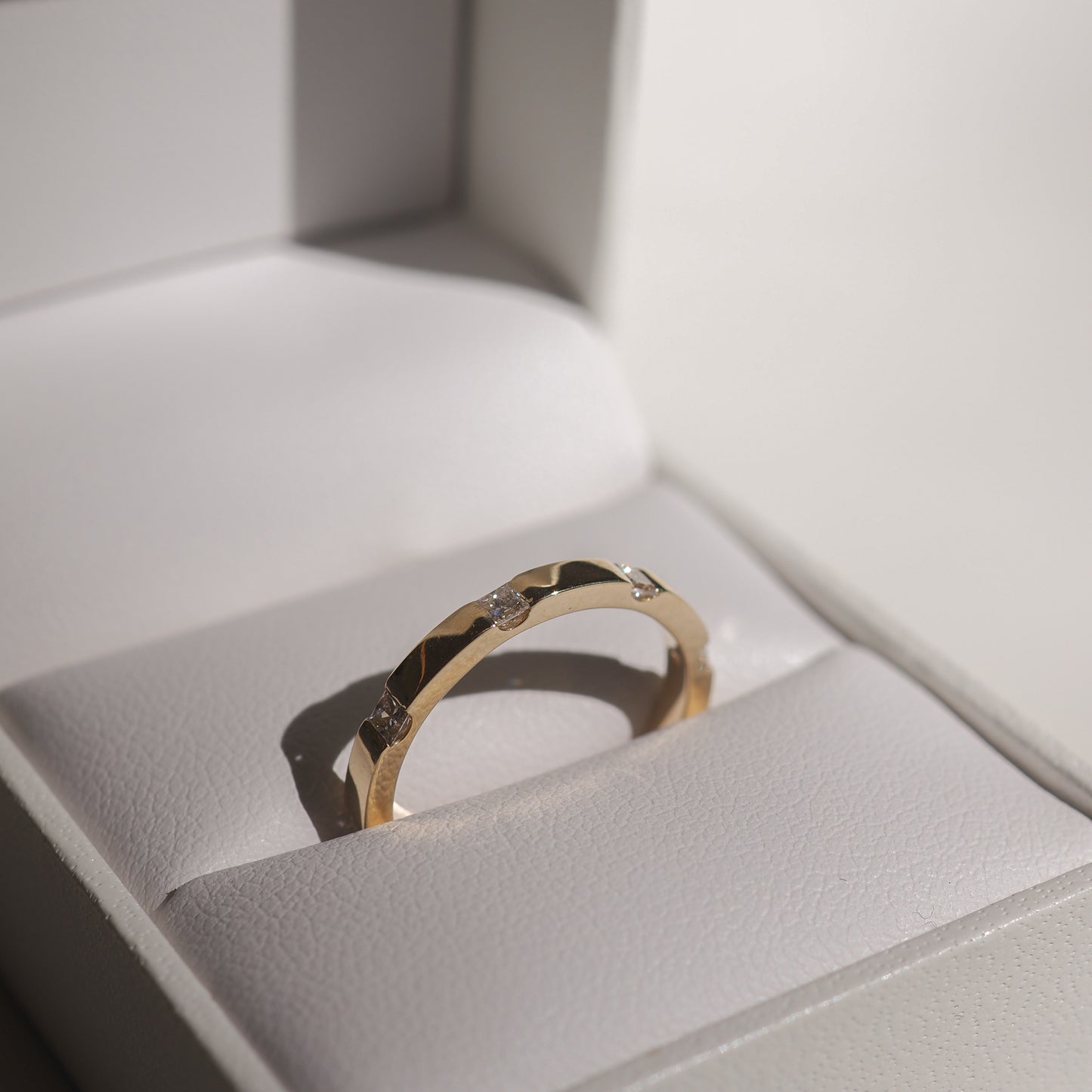 Gold ring with diamond accents in a white jewellery box, captured in soft lighting, highlighting its elegant design and luxury appeal.