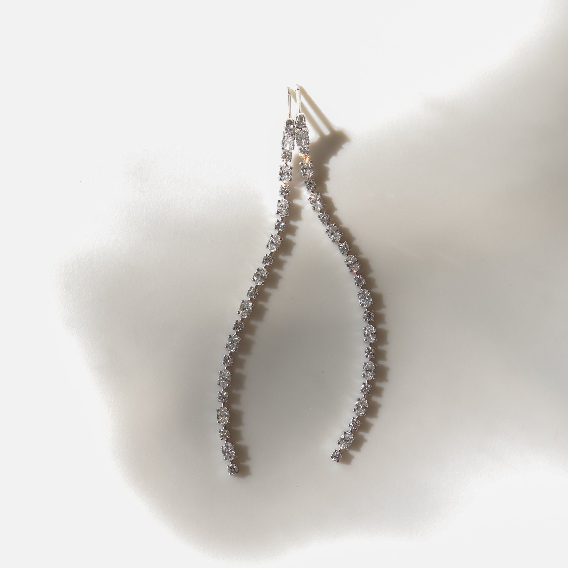 Elegant curved diamond earrings on a soft, diffused background, showcasing luxury jewellery design and sparkling gemstones.