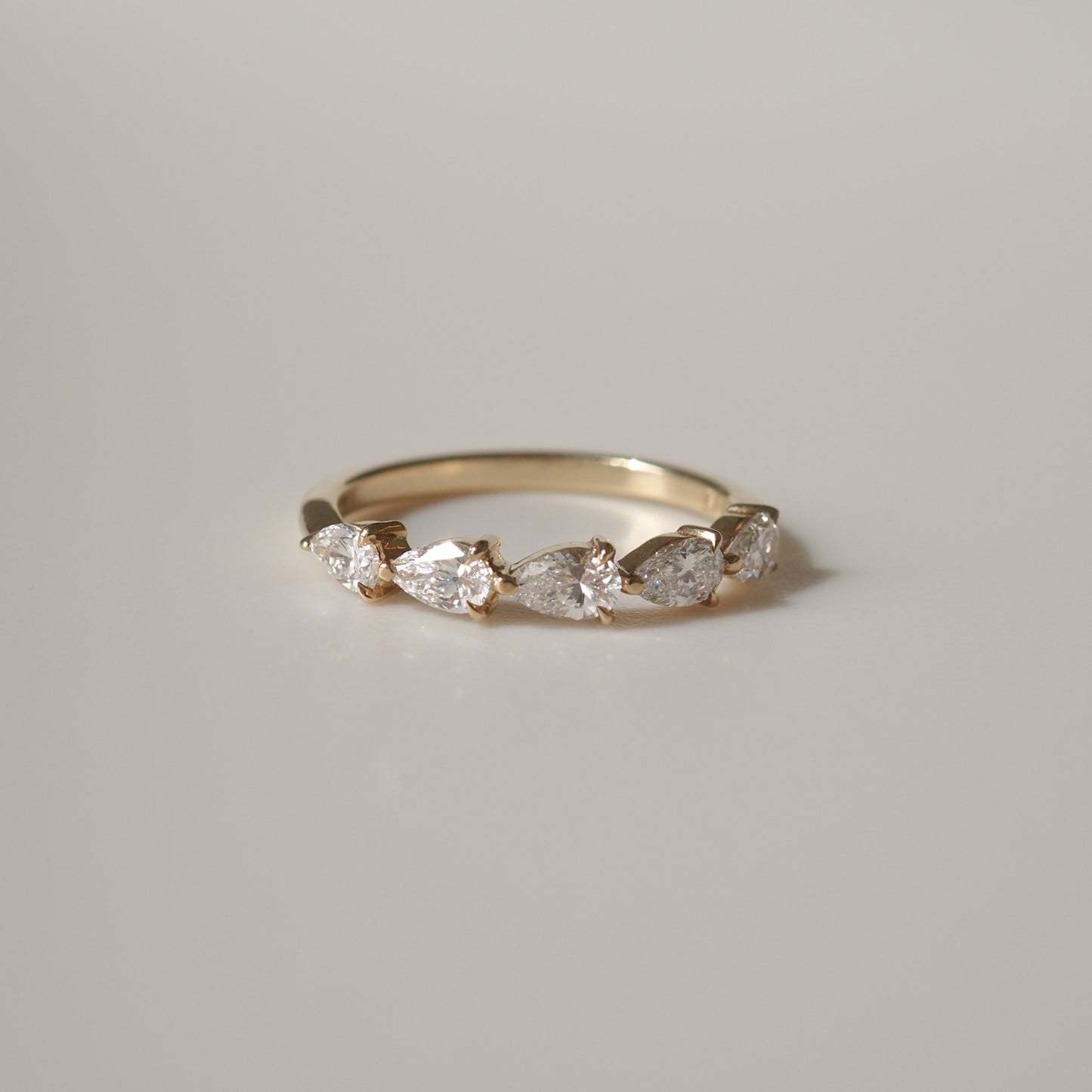 Gold ring with five pear-shaped diamonds set in a row, displayed on a neutral background. Luxury jewellery, elegant design.