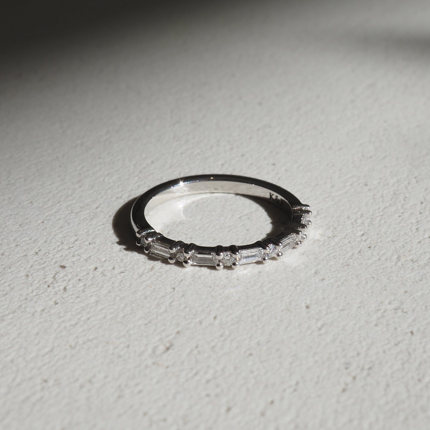 Elegant diamond ring with baguette-cut stones on a white surface, casting a soft shadow, symbolising luxury jewellery.