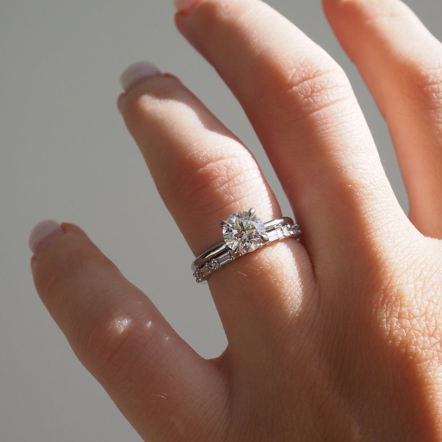 Hand displaying a luxurious diamond engagement ring and wedding band set in white gold, catching light against a neutral background.